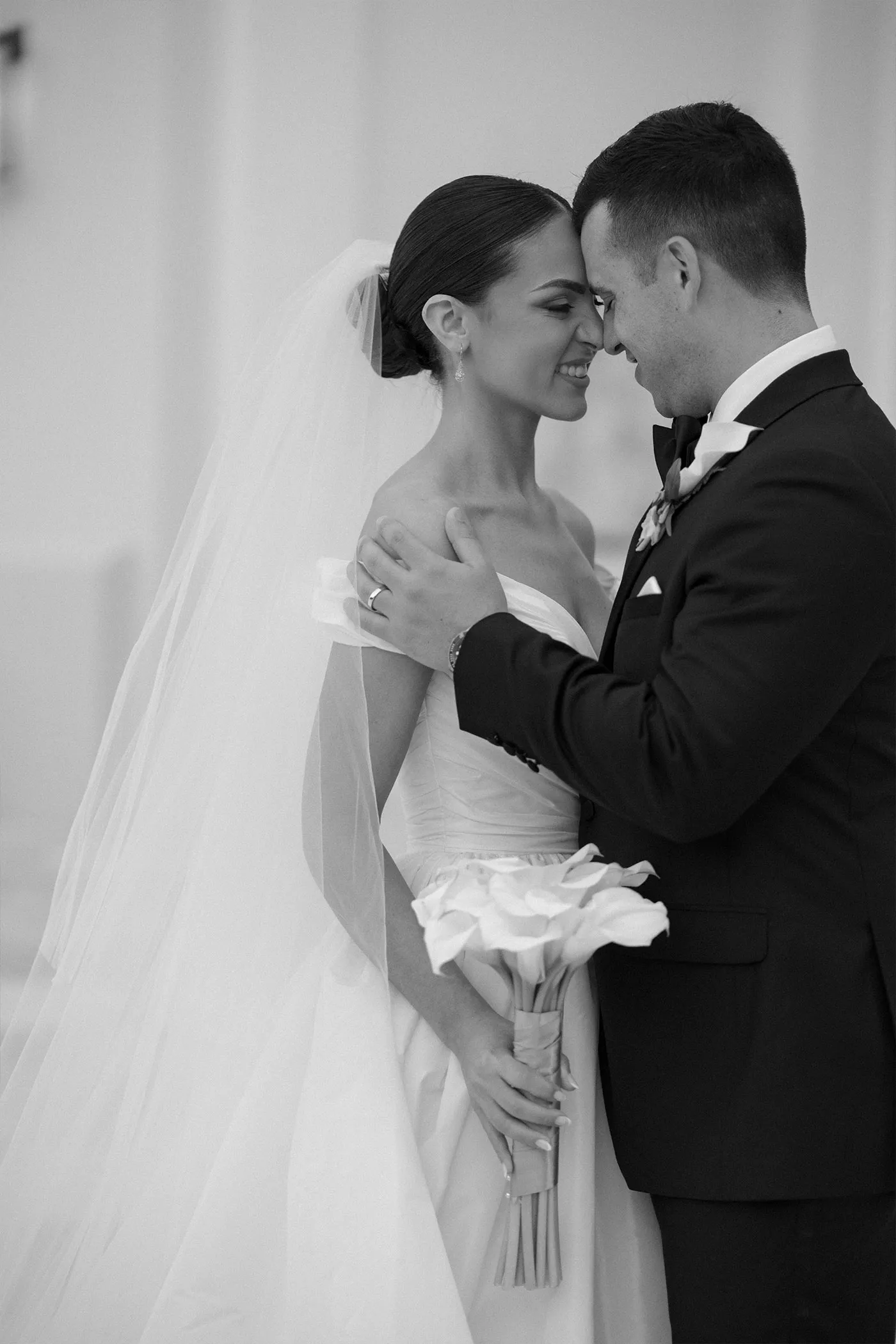 Bride and groom forehead to forehead, her calla lily bouquet between them