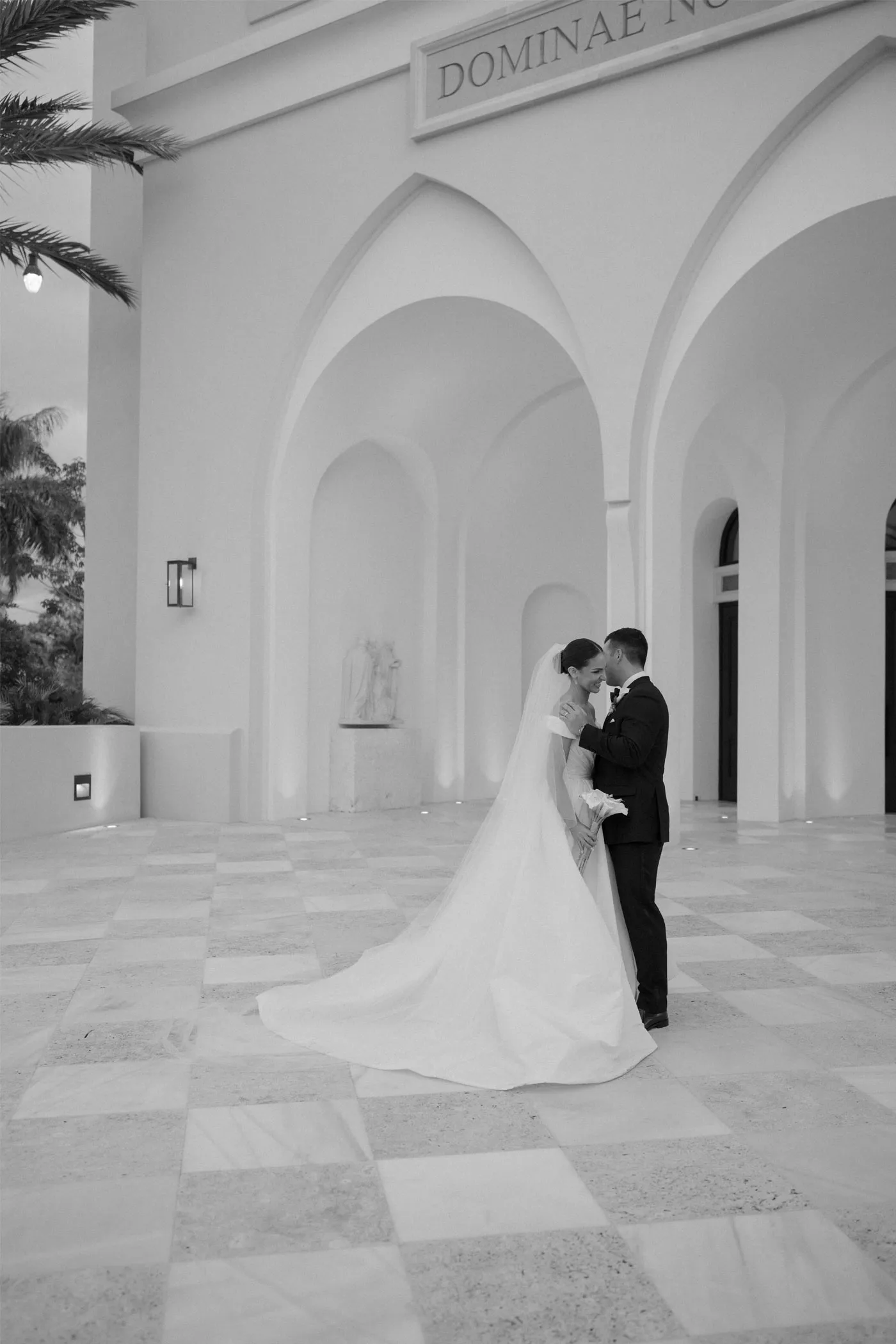 Bride and groom close together under white arches on a checkered stone terrace