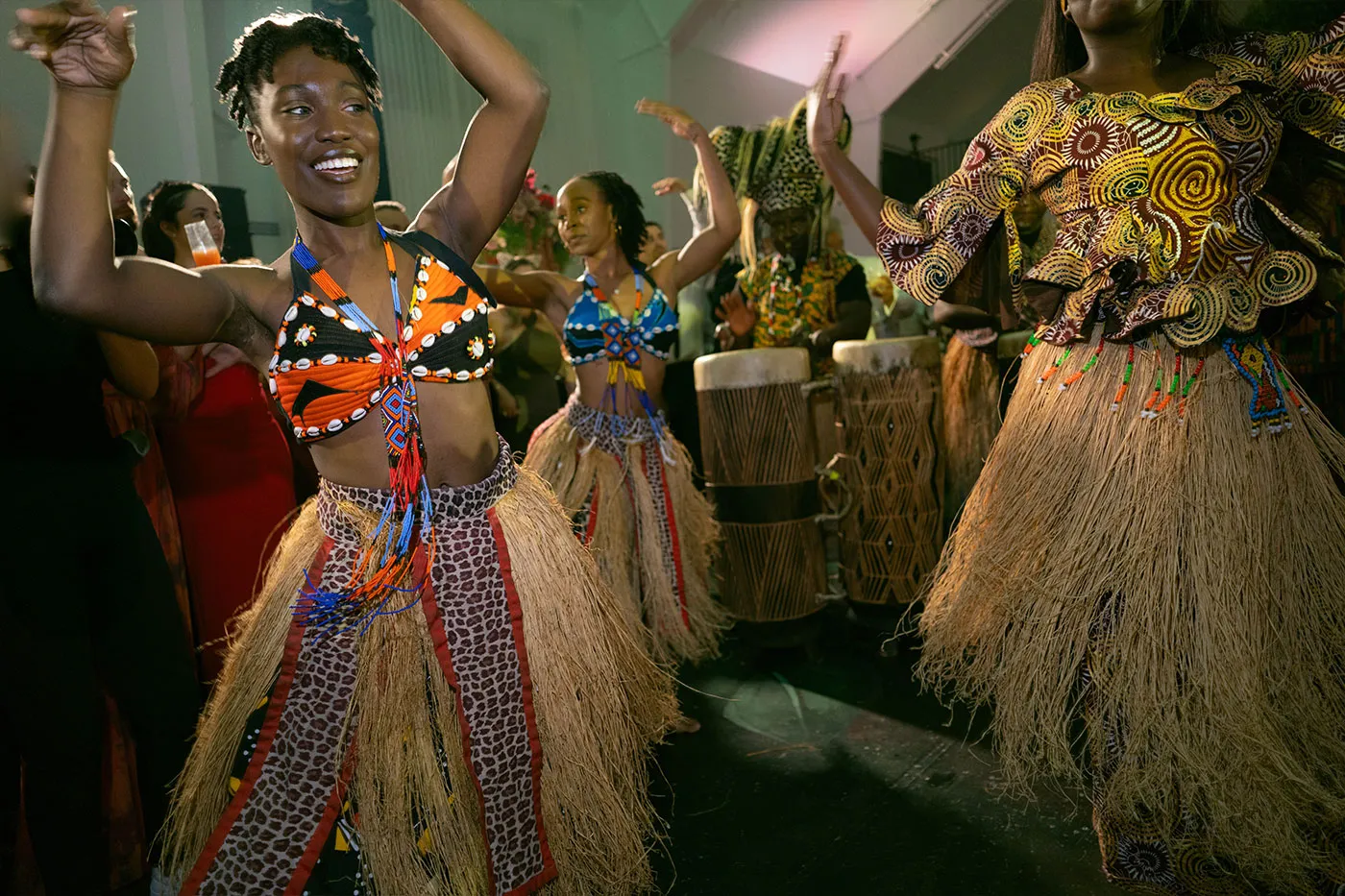 Dancers in beaded tops and raffia skirts performing with drummers at a reception