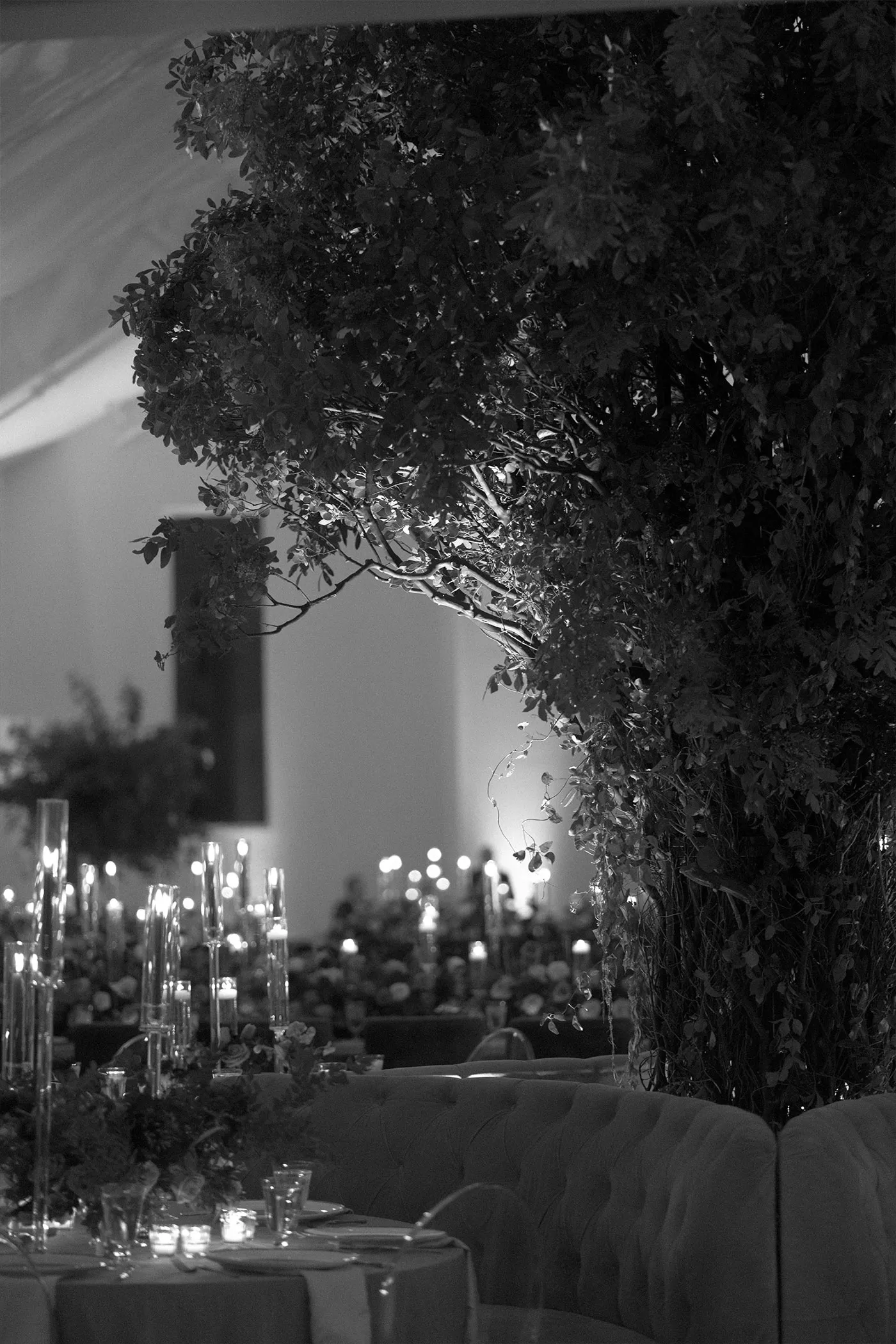 Tall foliage installation over candlelit reception tables, black and white