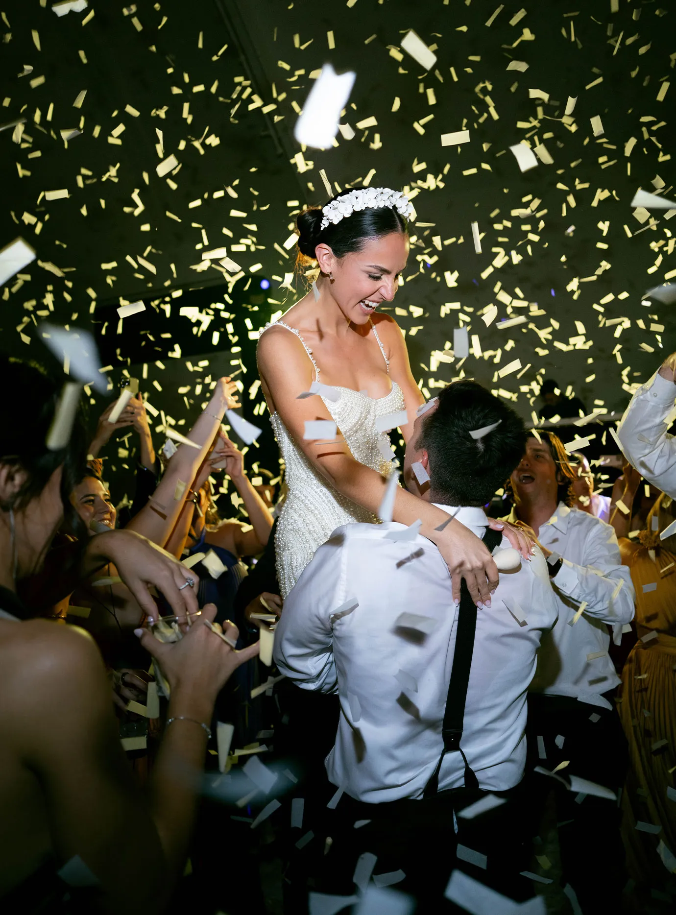 Groom lifting the laughing bride on the dance floor as gold confetti falls