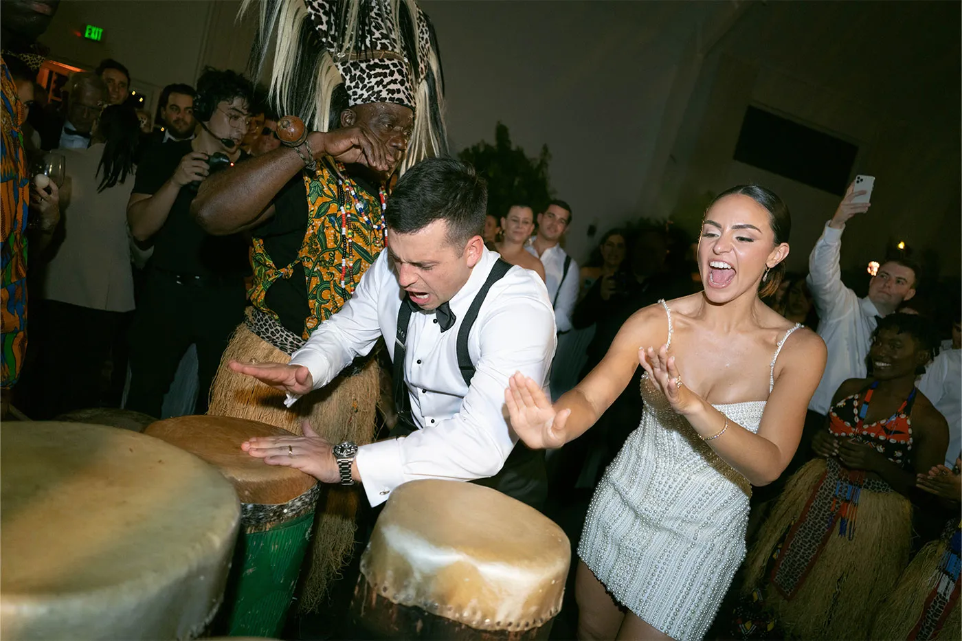 Groom playing a drum beside a costumed drummer as the bride cheers