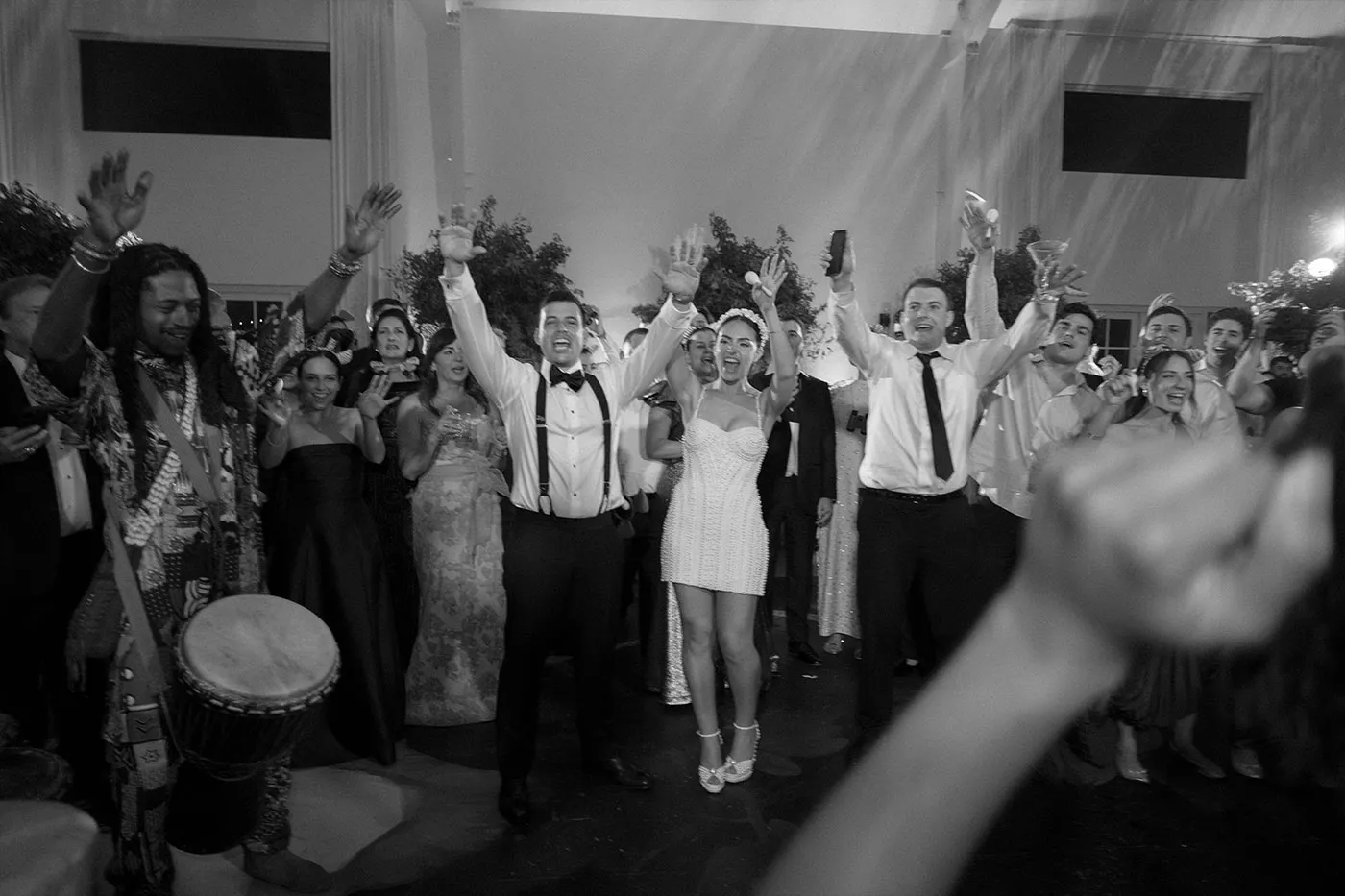 Bride and guests cheering with arms raised on the dance floor, drummer at left