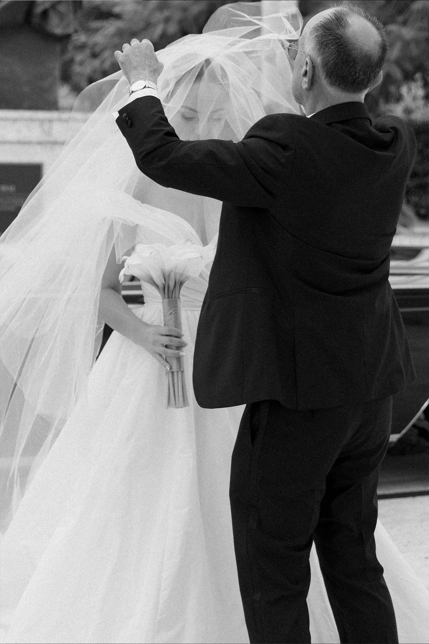 Older man in a suit lifting the bride's veil as she holds her bouquet, black and white
