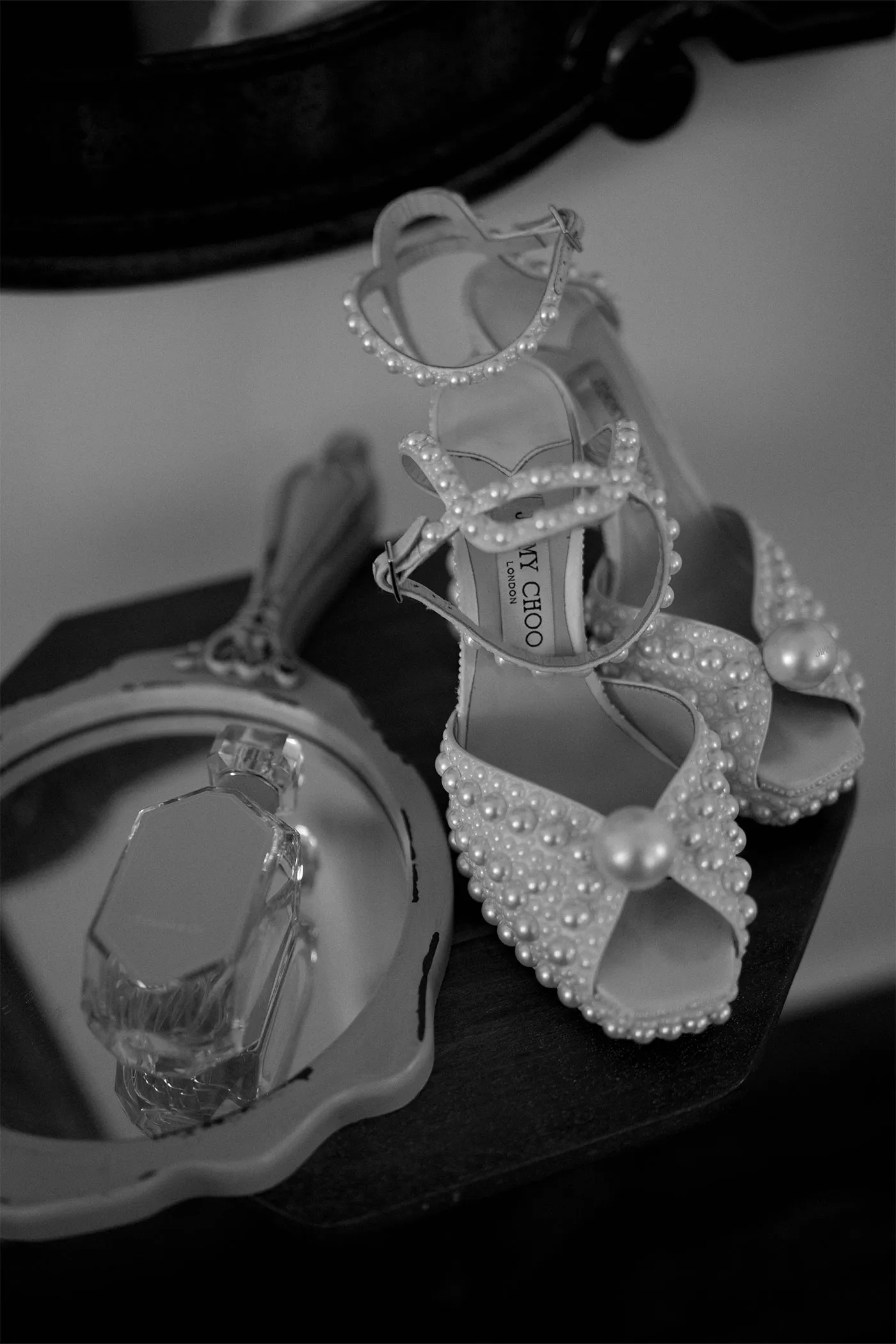 Pearl-covered bridal sandals beside a cut-glass perfume bottle on a dresser