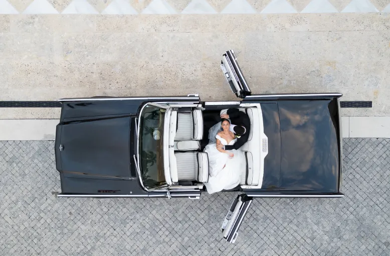 Overhead view of a bride and groom seated in a convertible car with its doors open
