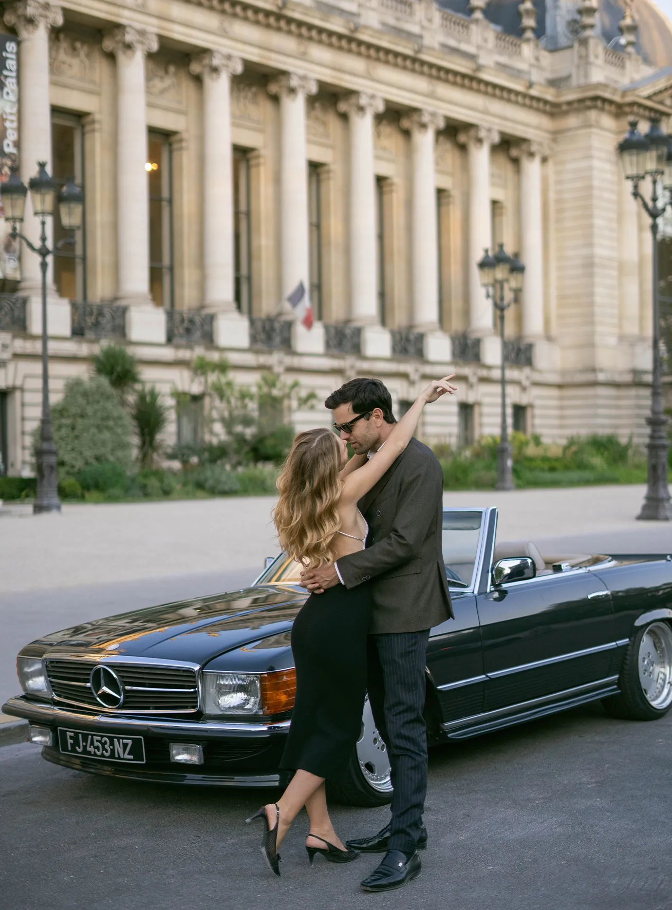 Couple embracing beside a black vintage convertible outside the Petit Palais