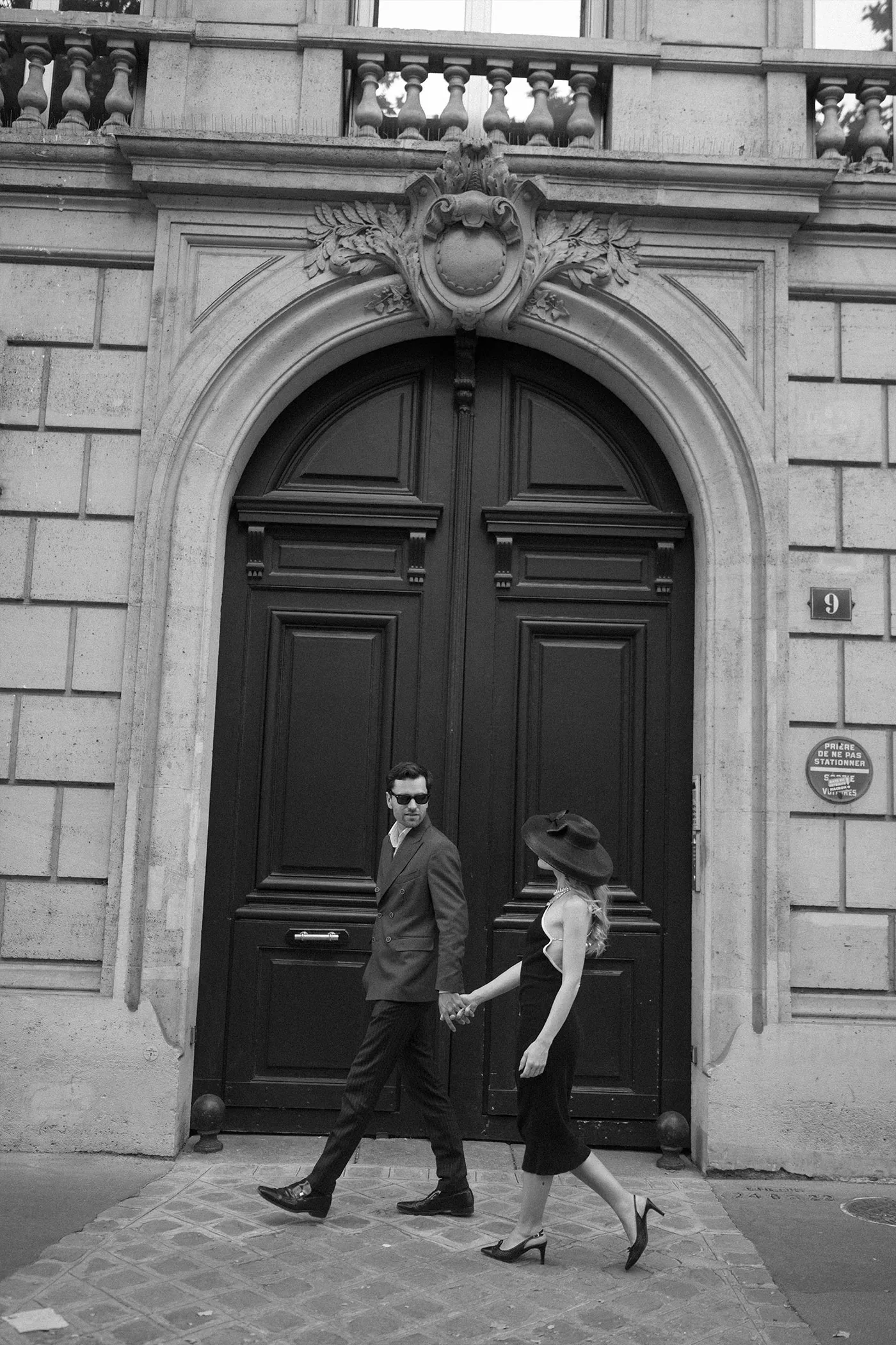 Couple in black tie walking hand in hand past a carved city doorway, black and white