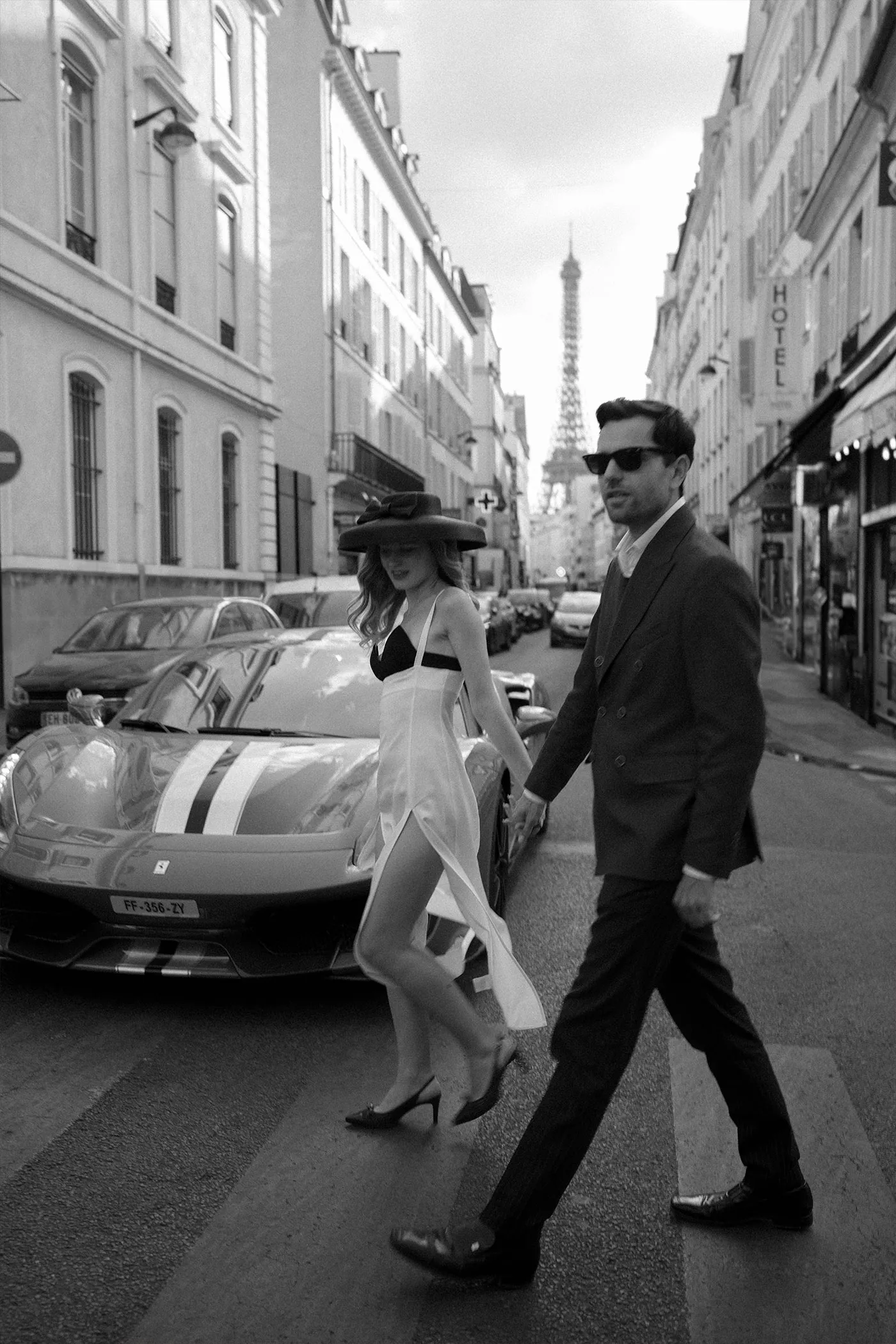 Couple crossing a Paris street past a sports car, Eiffel Tower in the distance