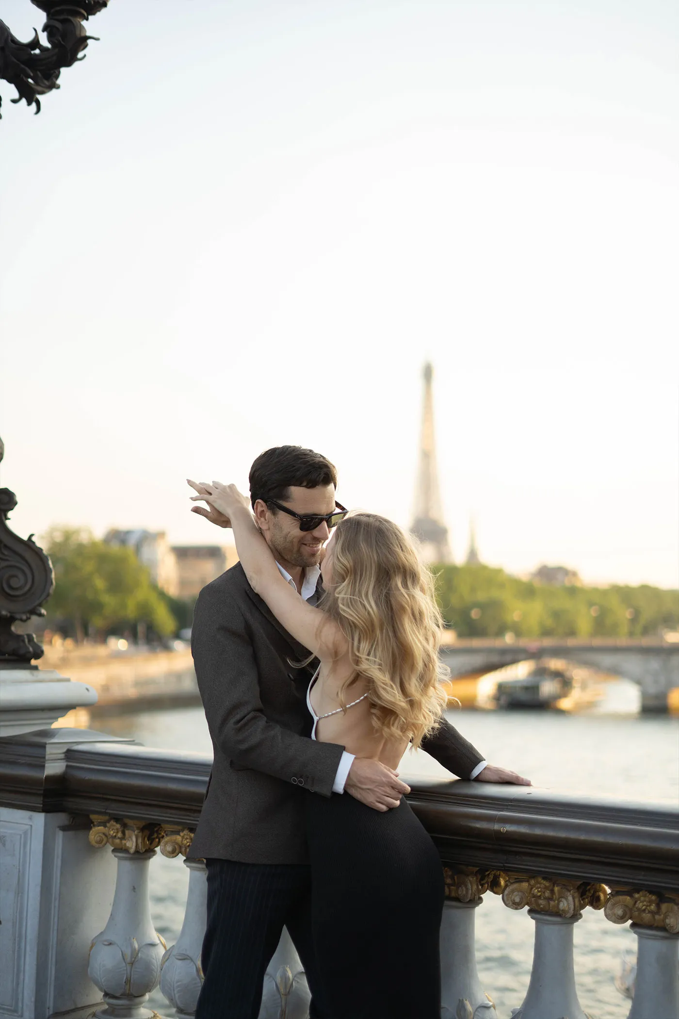 Couple embracing at a bridge railing with the Eiffel Tower beyond the river