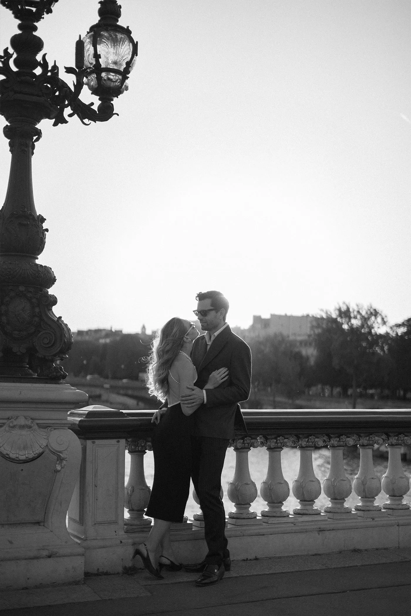 Couple embracing beside an ornate lamppost on a stone bridge balustrade