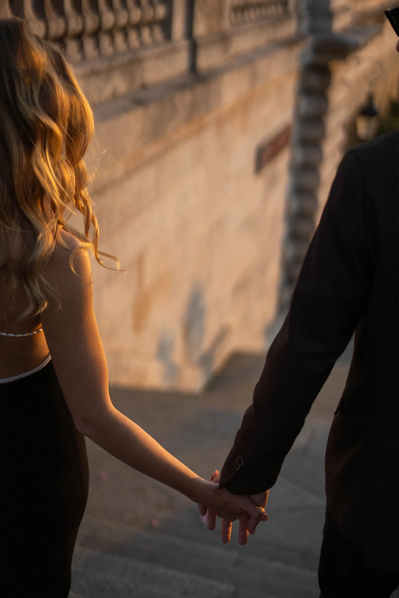 Couple holding hands as they walk down stone steps in golden evening light