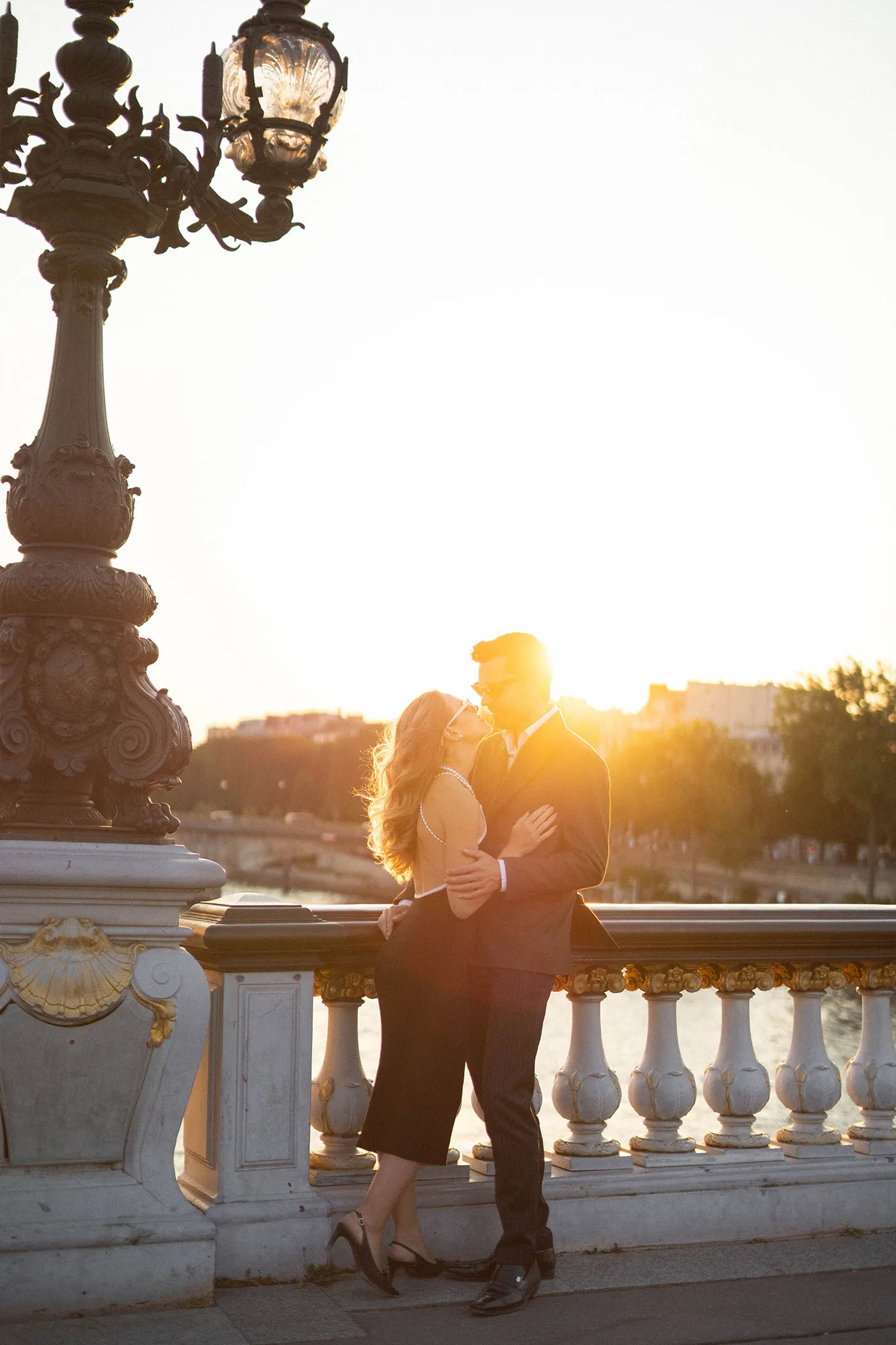 Couple kissing on a bridge, backlit by the low sun over the river