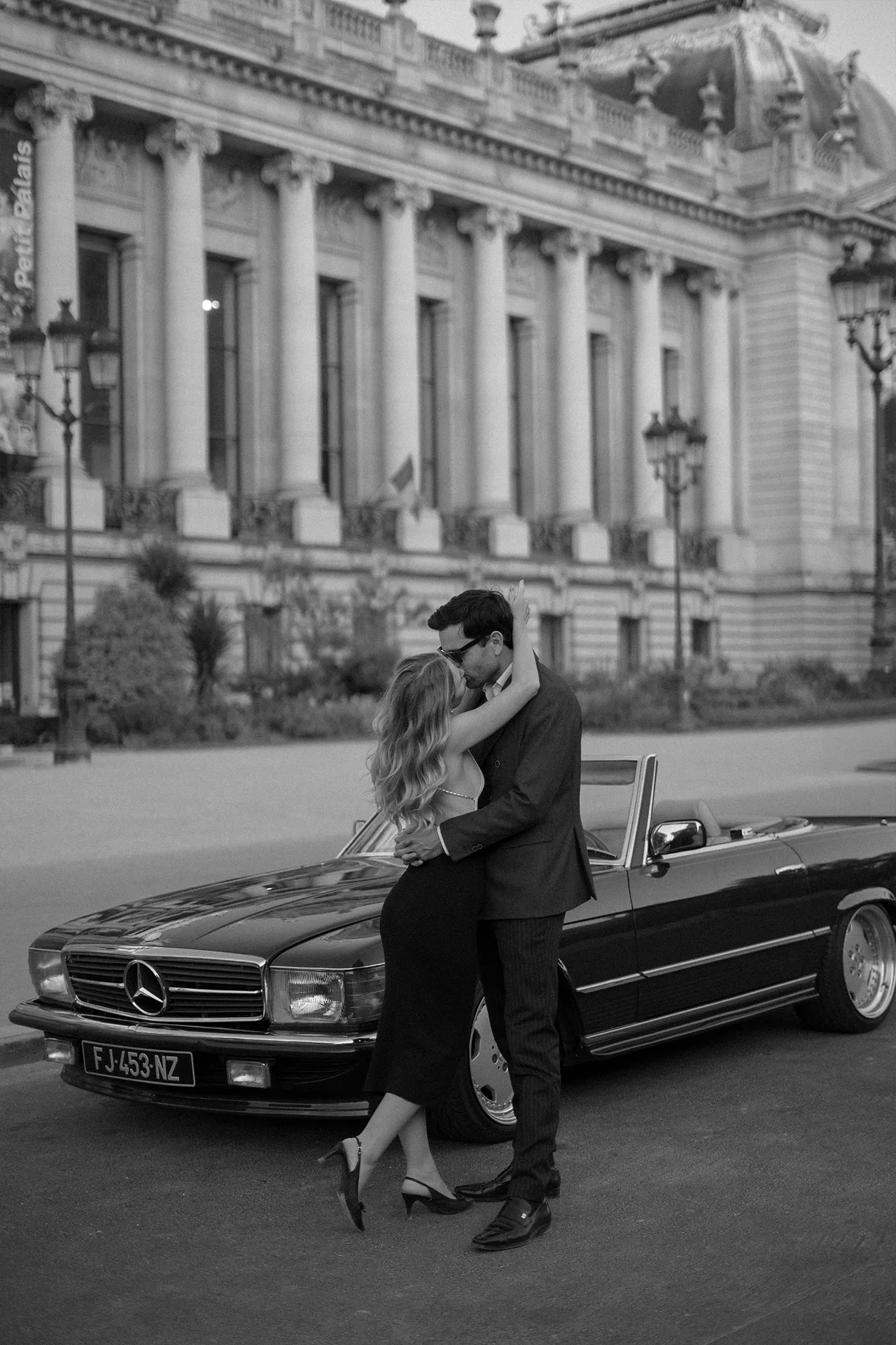 Couple kissing against a vintage convertible outside a columned palace, black and white
