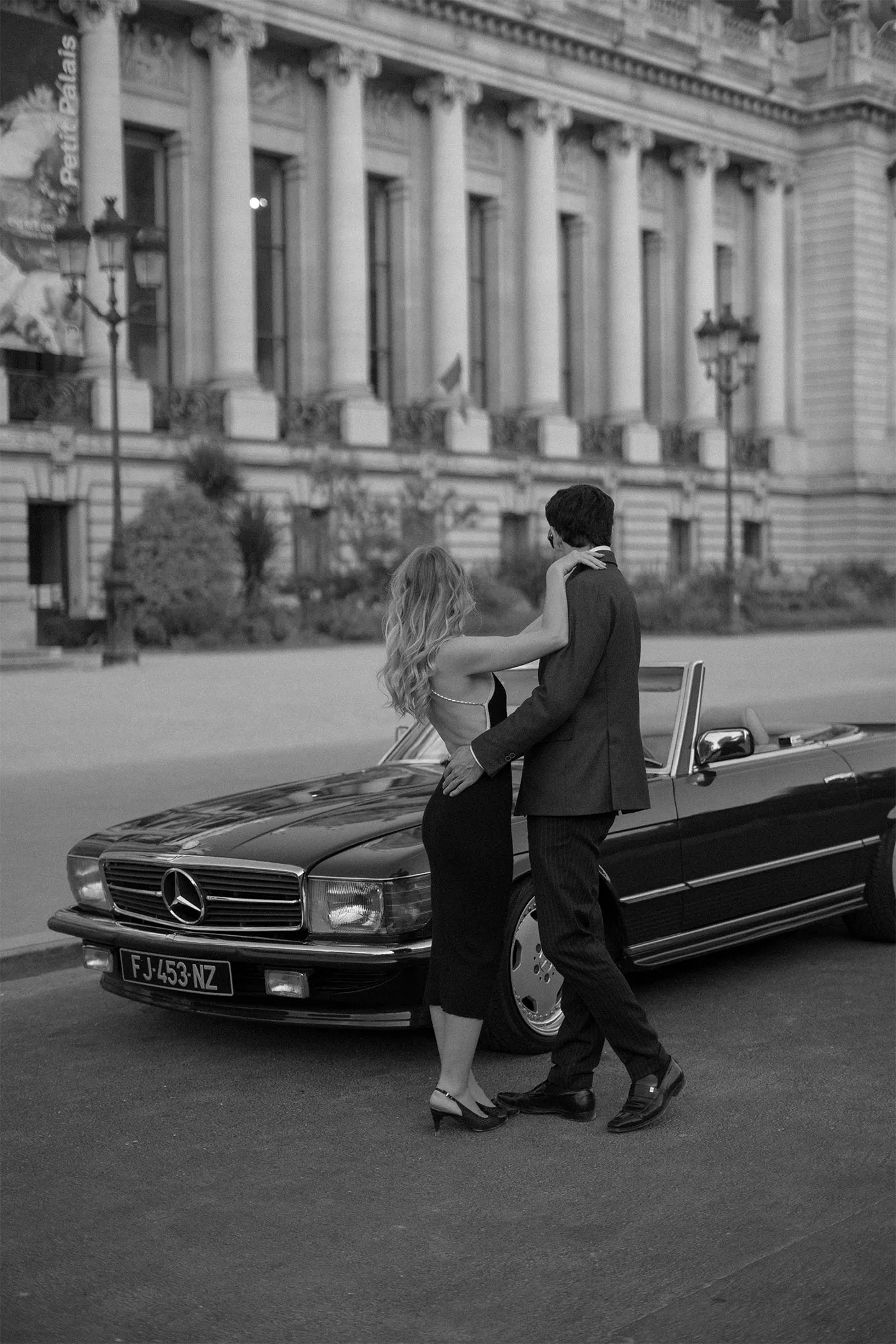 Couple in evening dress leaning together on a vintage convertible on a city street