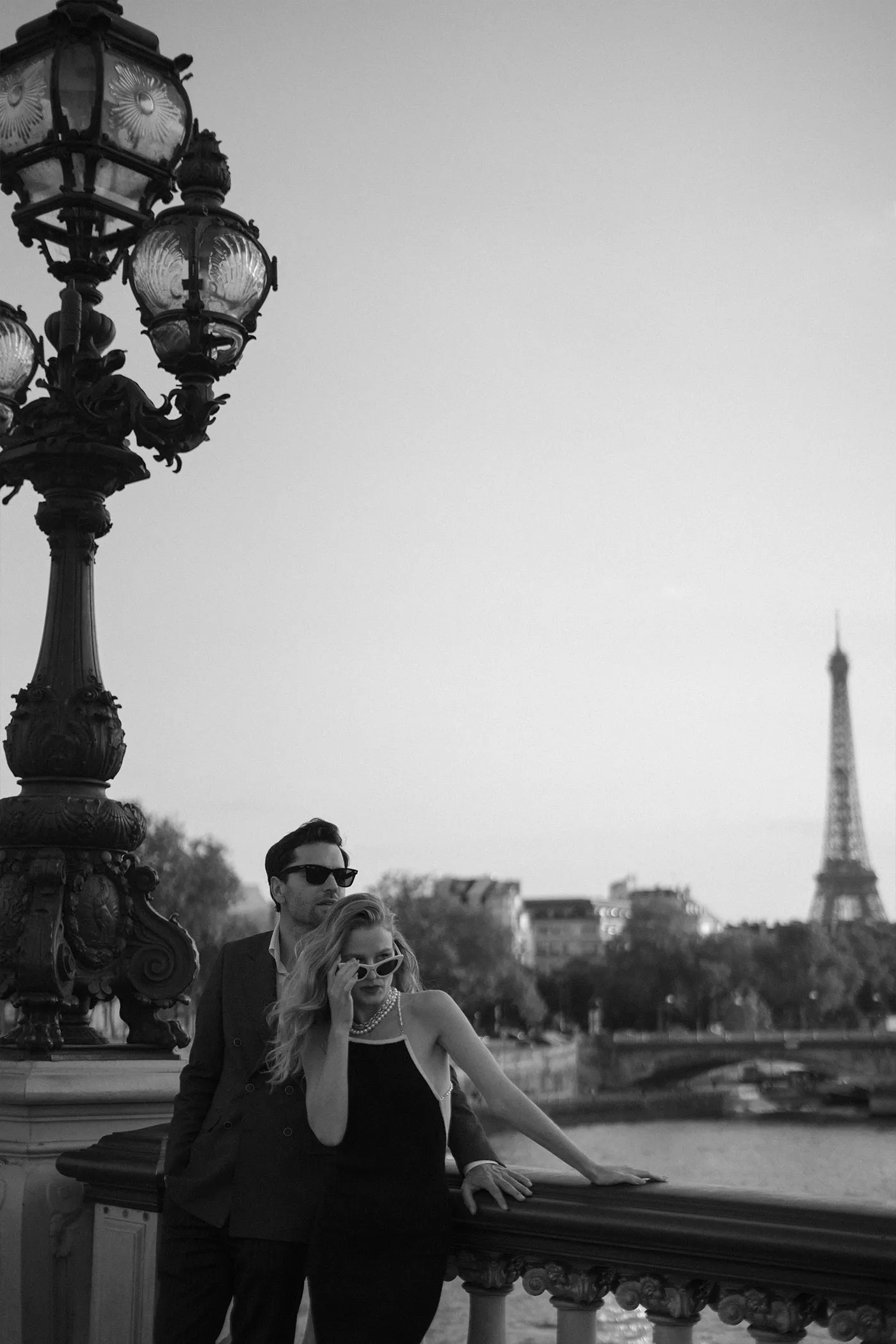 Couple in sunglasses leaning on a bridge railing with the Eiffel Tower behind
