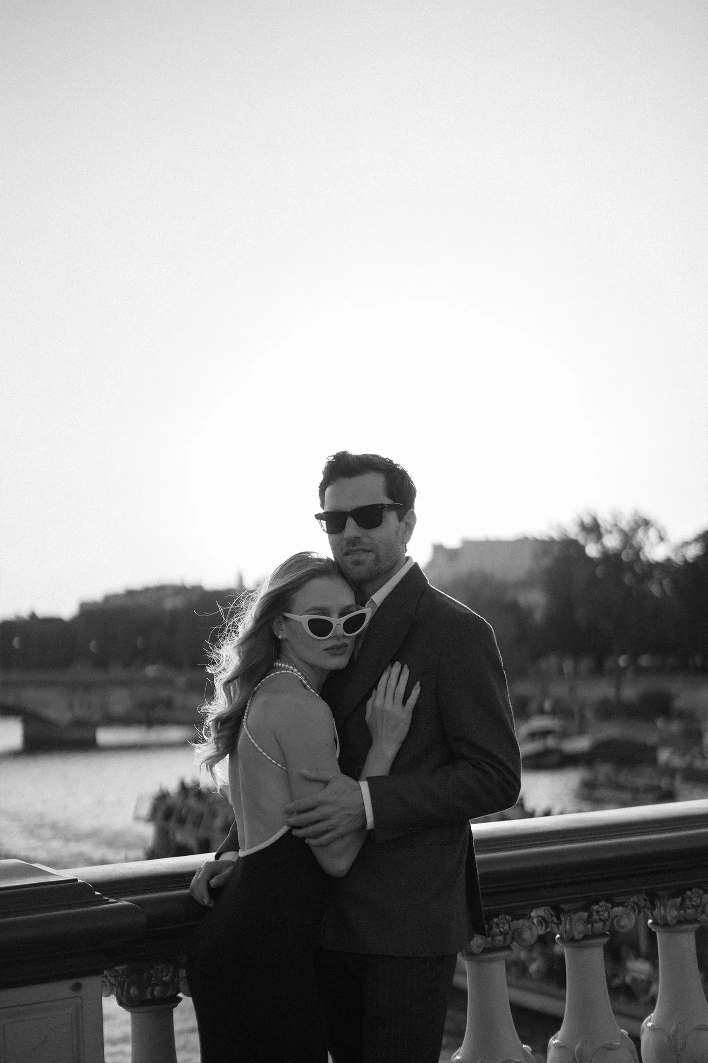 Couple in sunglasses embracing against a bridge railing above a river