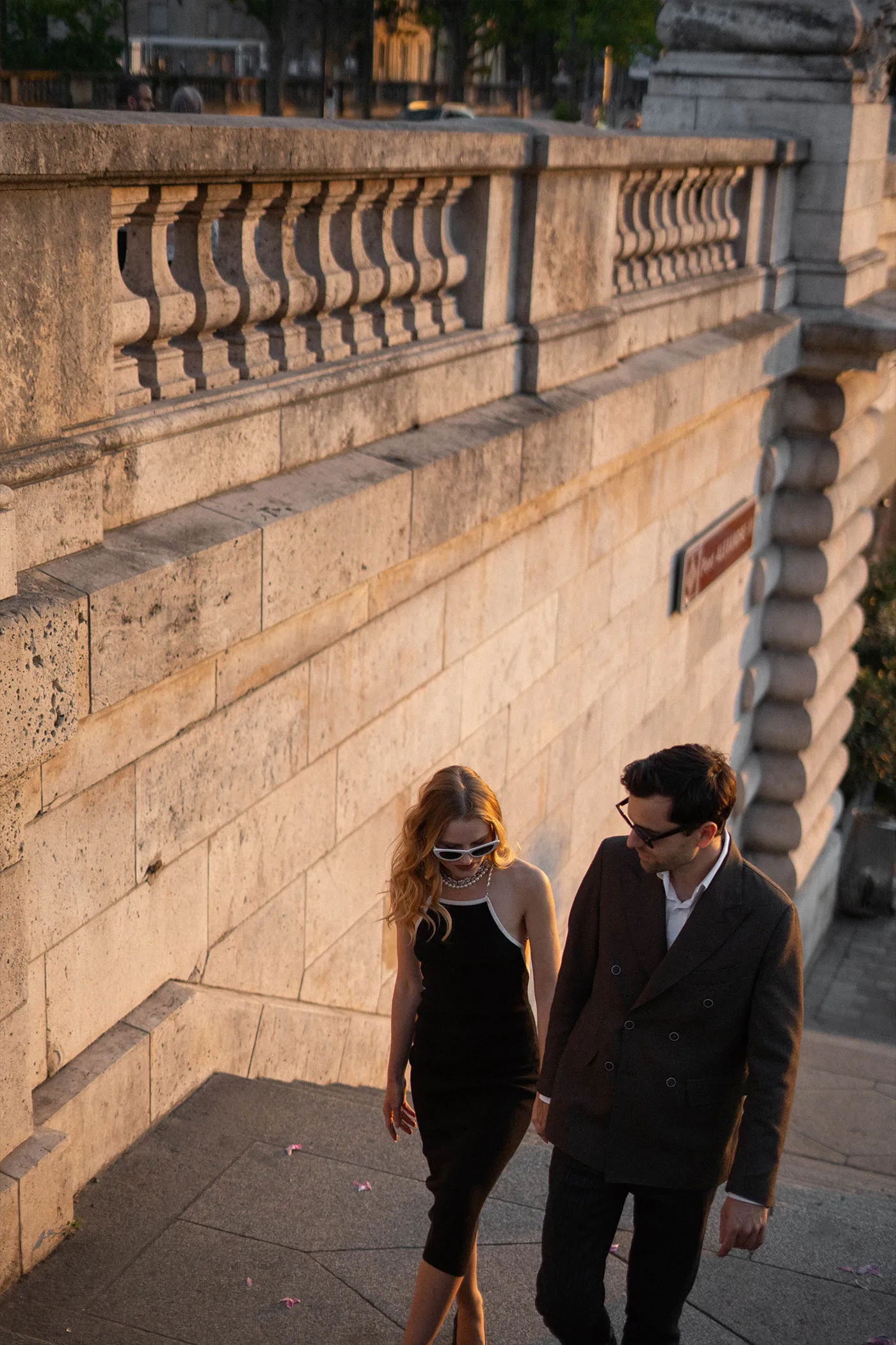 Couple in sunglasses walking along a stone embankment wall in low evening sun