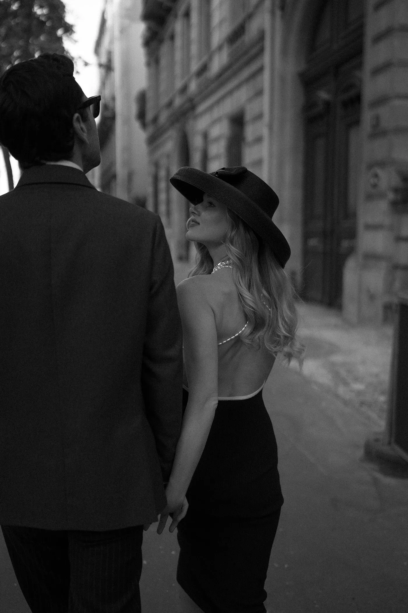 Woman in a wide-brimmed hat glancing back while walking a city street hand in hand