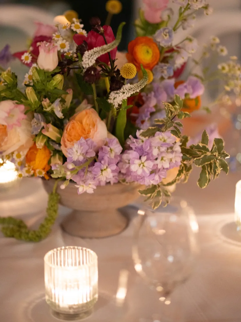 Reception centrepiece of roses, ranunculus and stock beside a lit candle