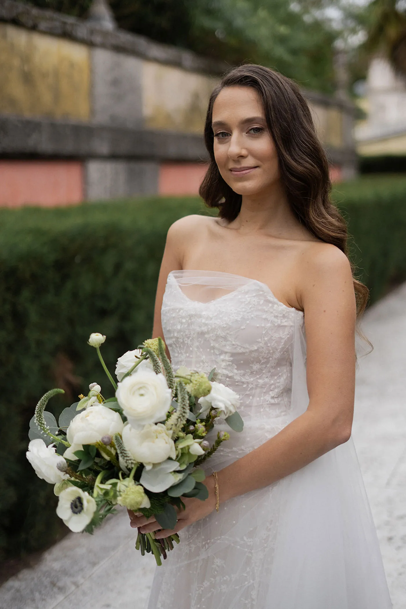 Bride in a strapless embroidered gown holding a white ranunculus and anemone bouquet