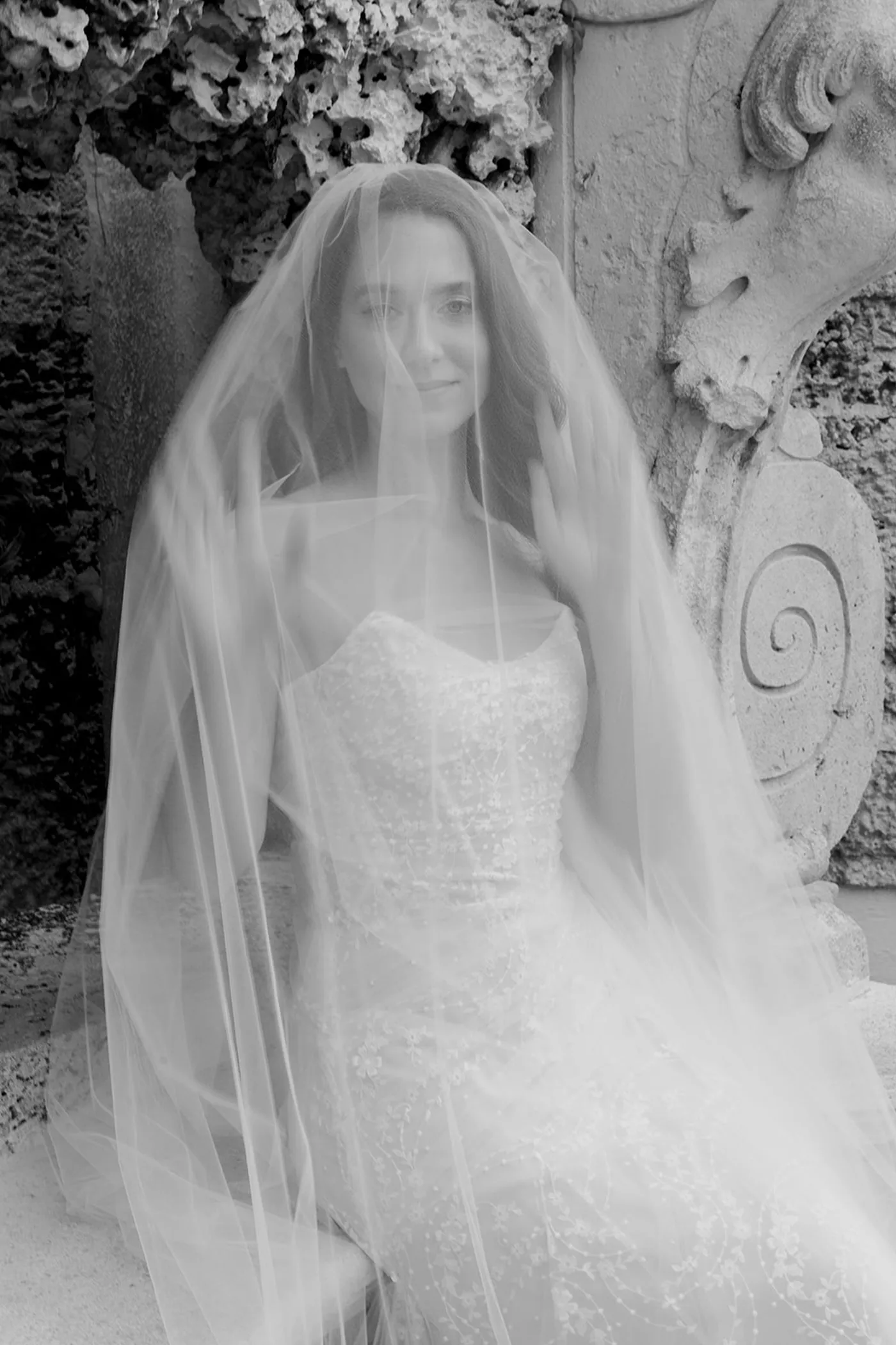 Bride seated against carved coral stone with a long veil drawn over her face