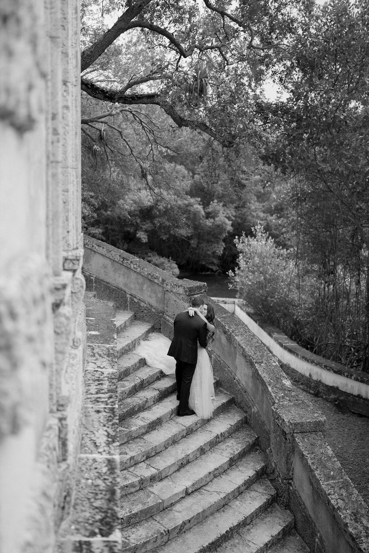 Bride and groom embracing on a curved stone garden staircase, black and white
