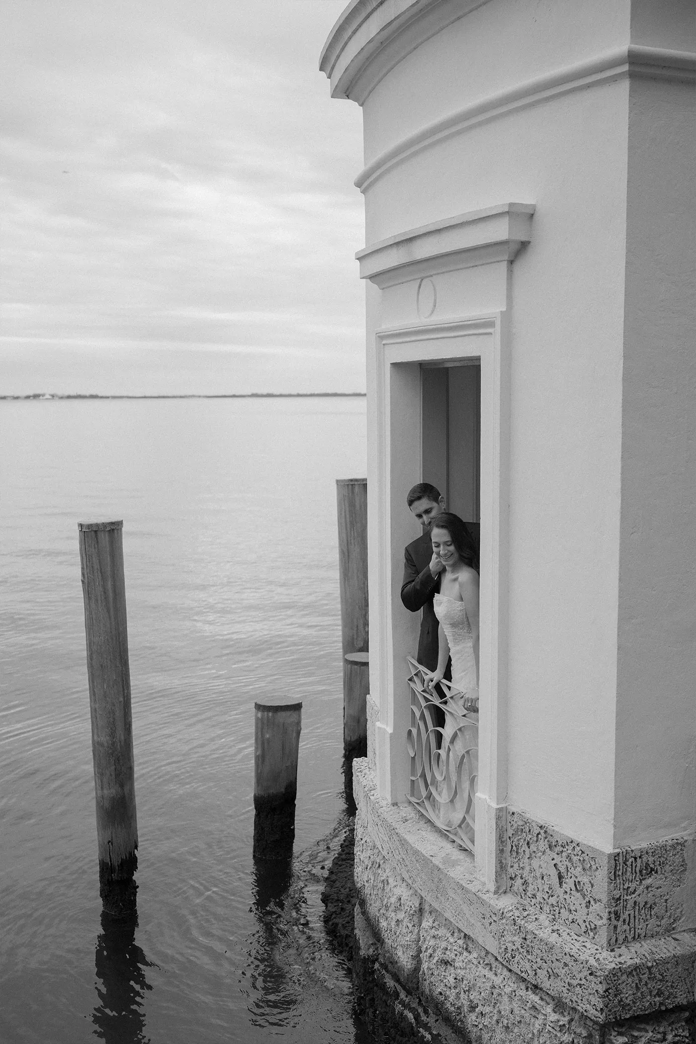 Bride and groom in a doorway above the water, mooring posts standing in the bay