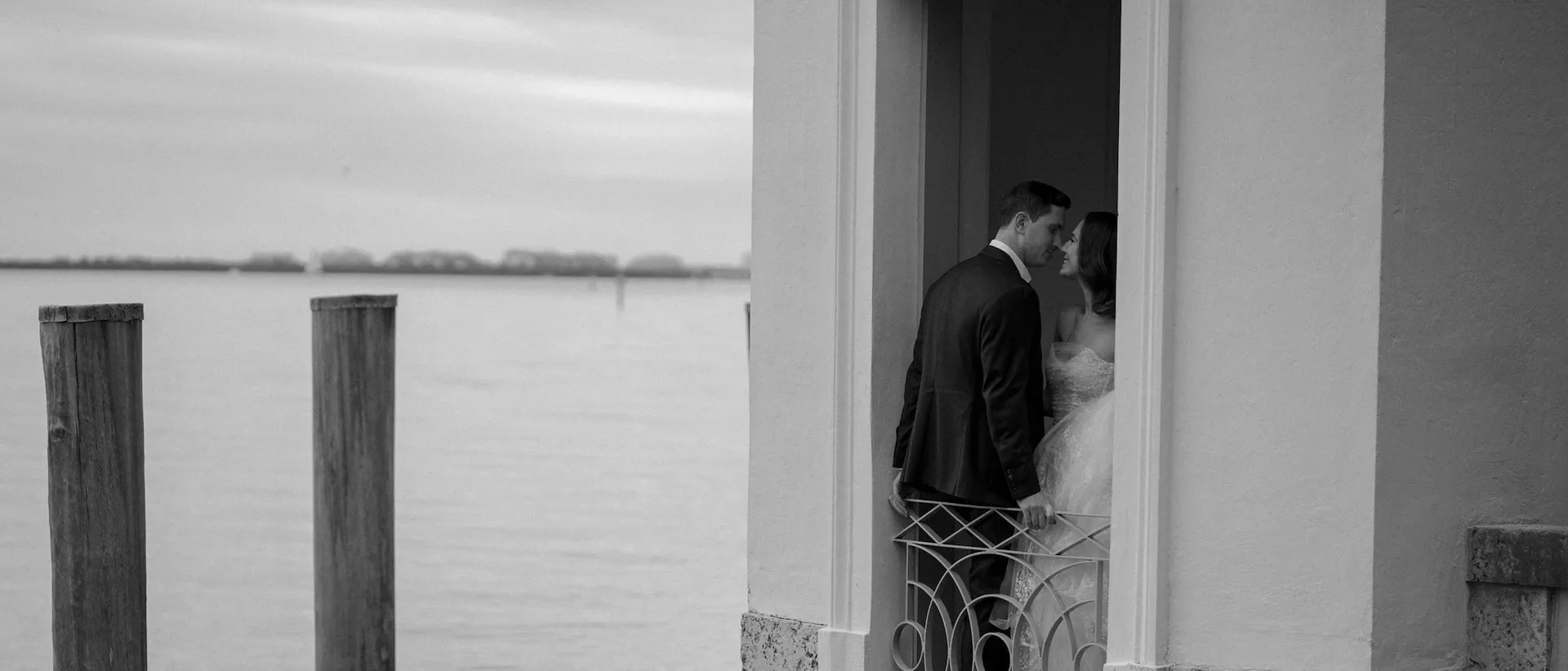 Bride and groom about to kiss in a doorway overlooking calm water and mooring posts