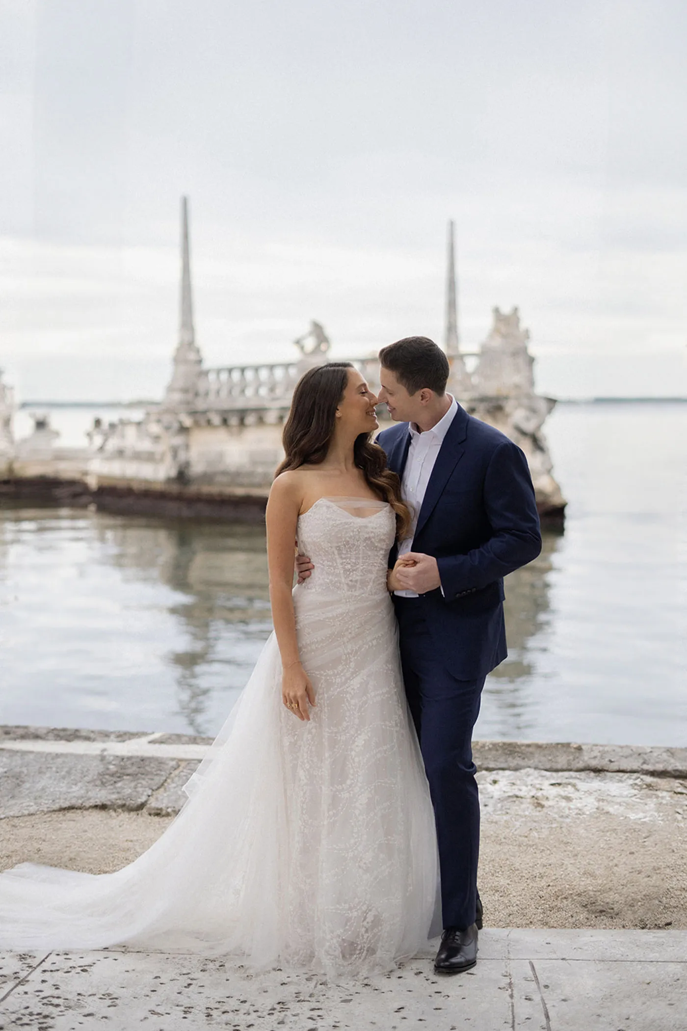 Bride and groom leaning in for a kiss on a waterfront stone terrace