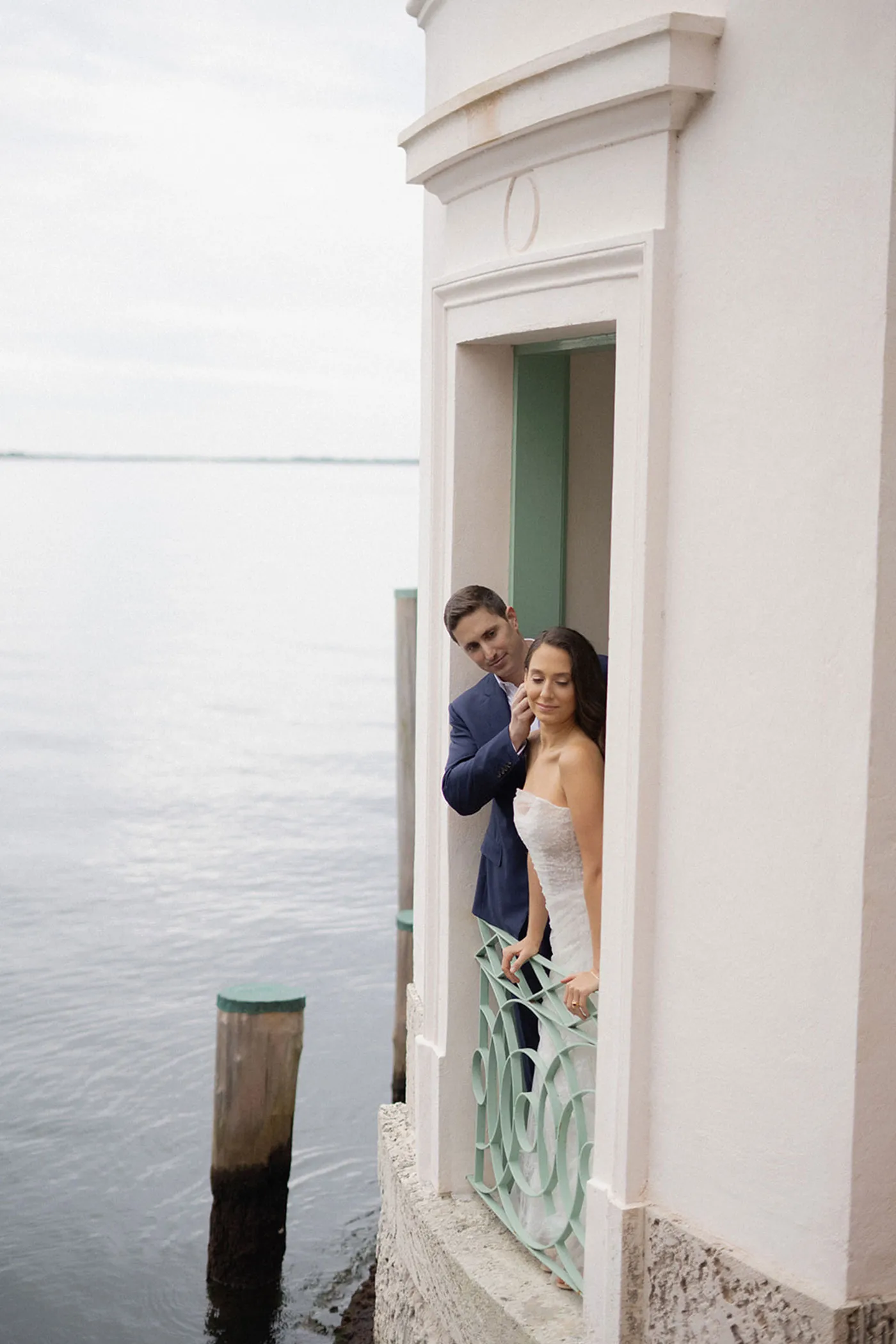 Bride and groom in a narrow doorway of a waterfront pavilion above the bay