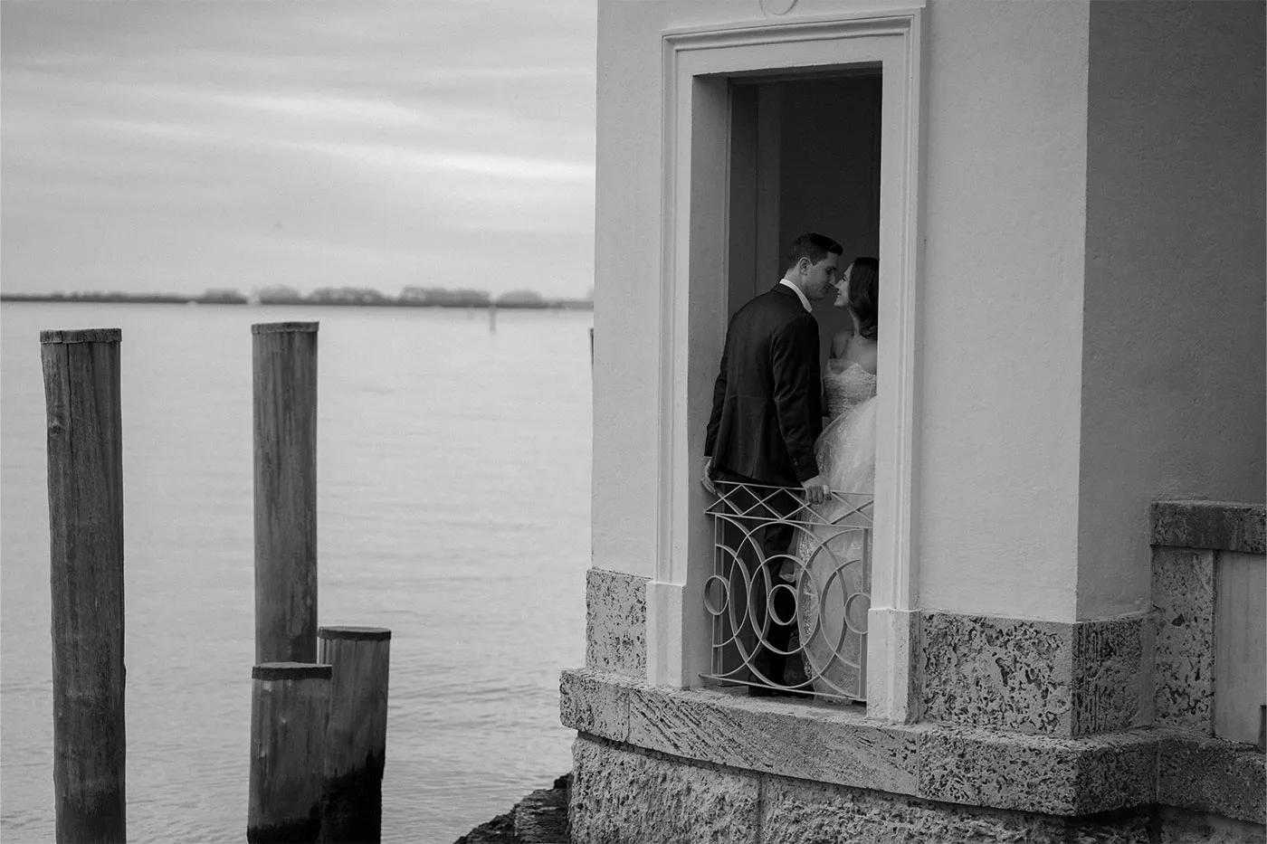 Bride and groom leaning close in a doorway of a waterfront pavilion, black and white