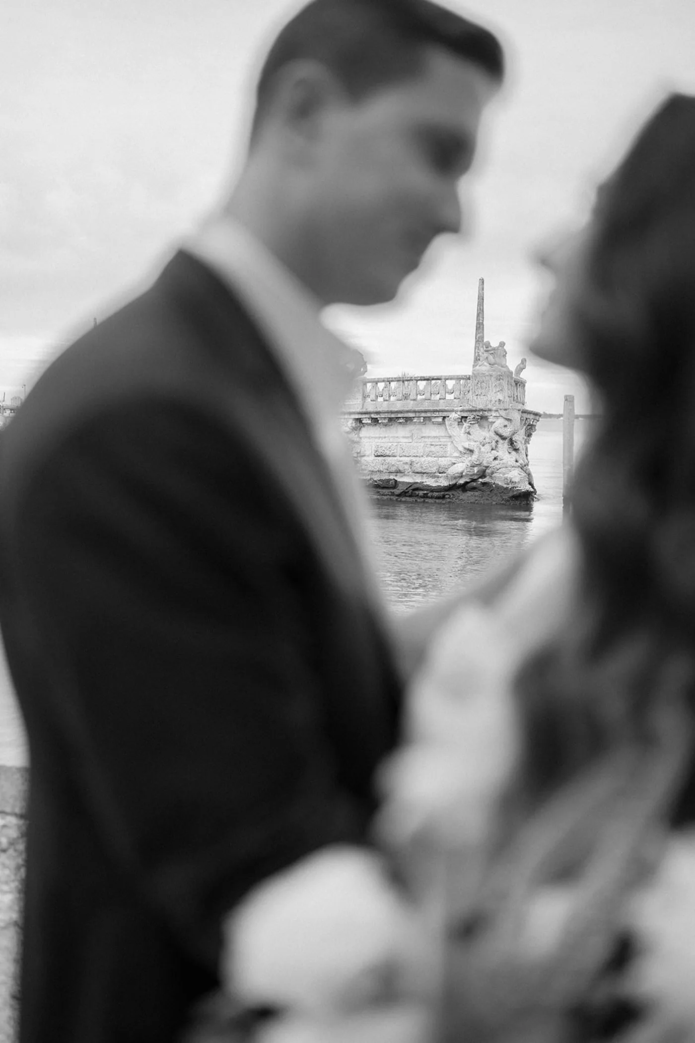 Bride and groom close together with a carved stone barge on the water behind