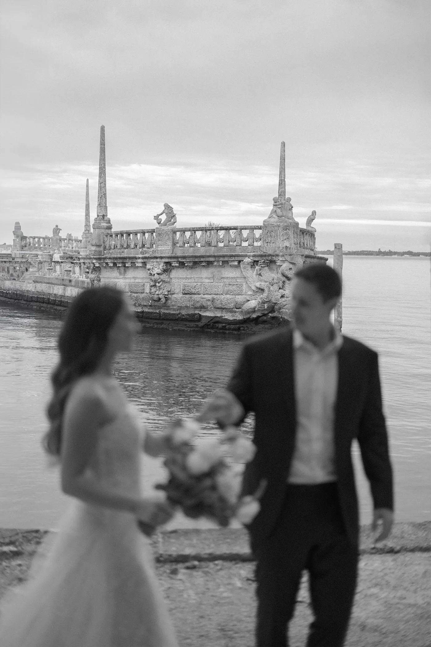 Couple walking past a carved stone barge on the water, seen out of focus