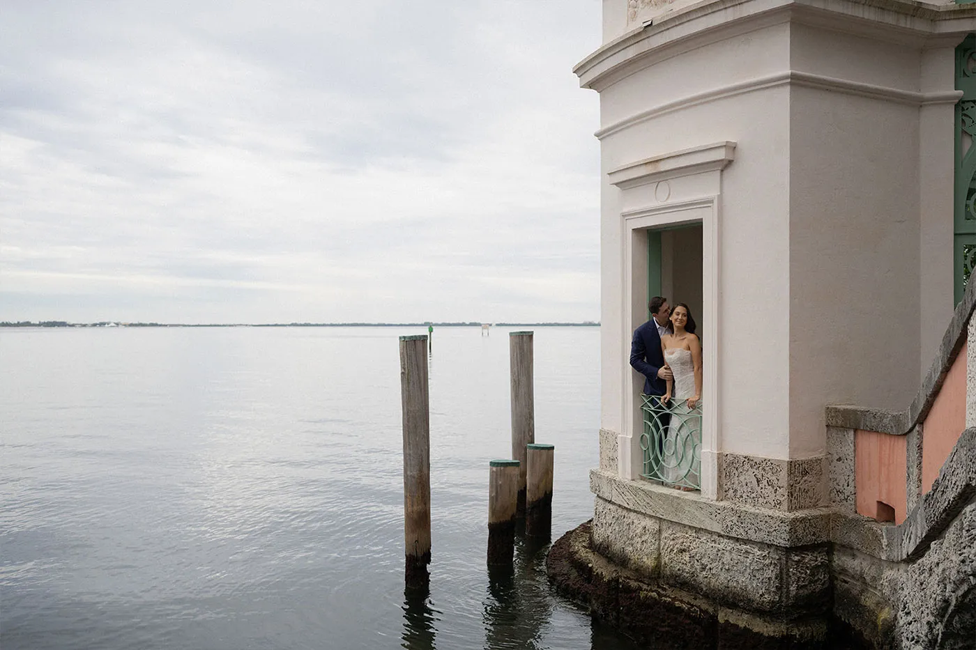Couple in a doorway of a stone pavilion at the water's edge, pilings in the bay