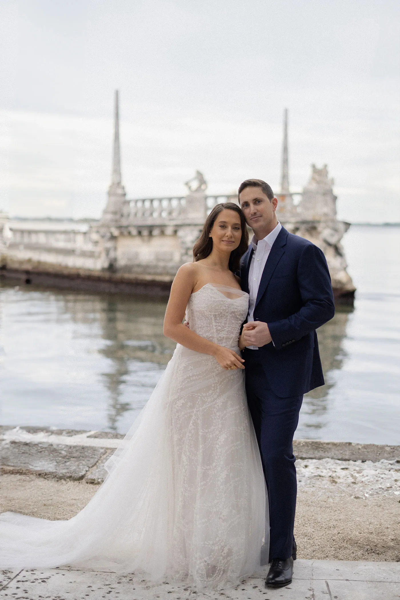 Bride and groom on a stone seawall with a carved stone barge behind them