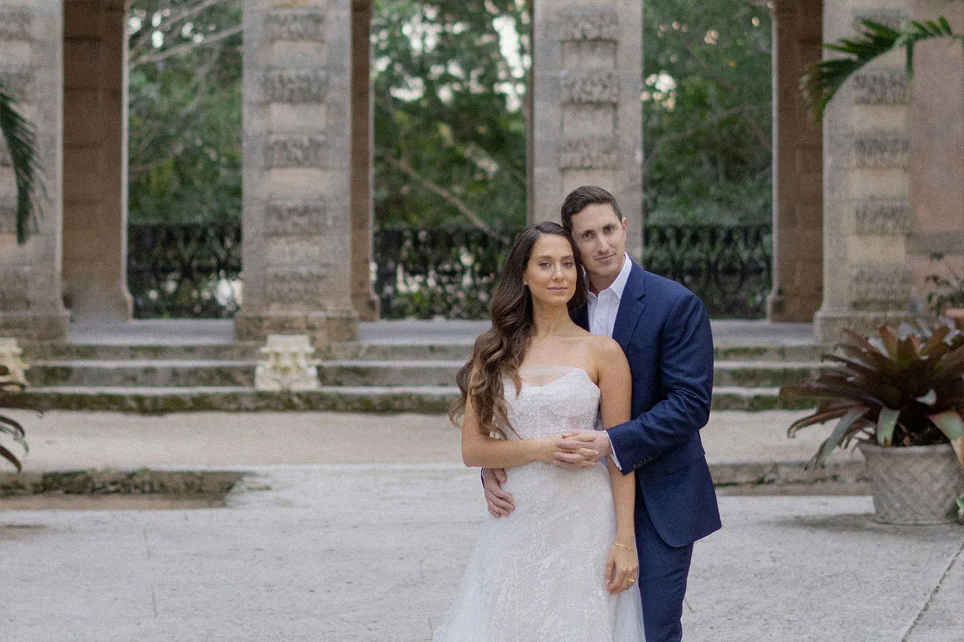 Groom holding the bride from behind in front of a stone colonnade