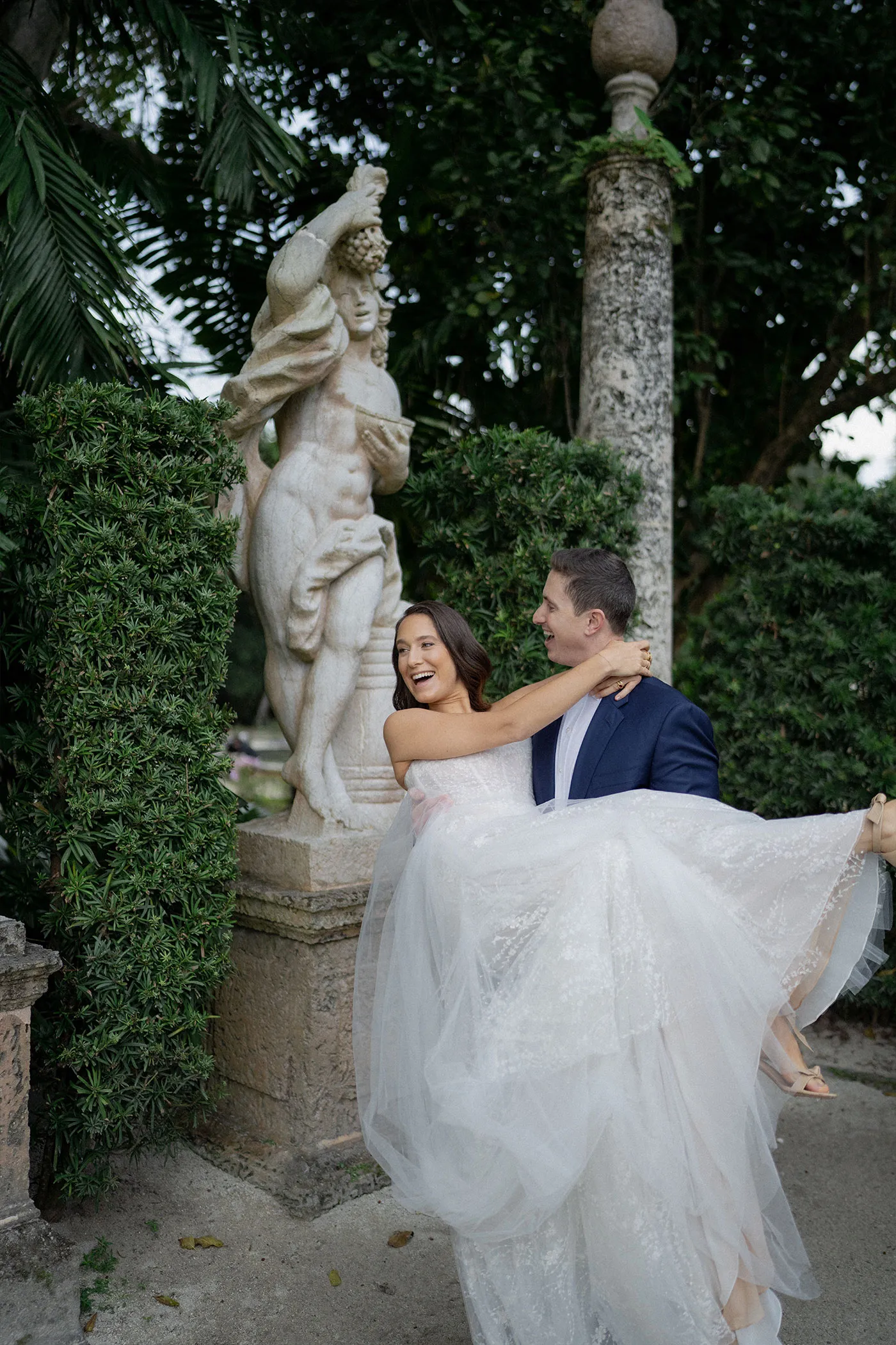 Groom lifting the laughing bride in his arms beside a garden statue