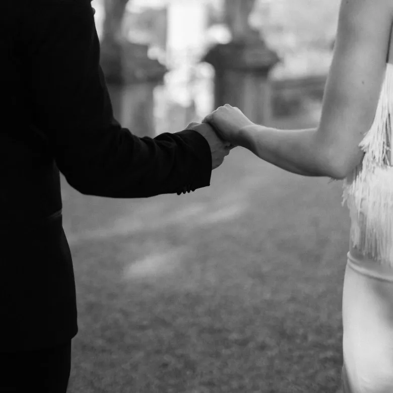 Close view of a groom and bride holding hands as they walk across a lawn