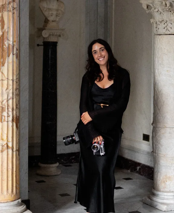 Photographer in a black slip dress holding two film cameras between marble columns