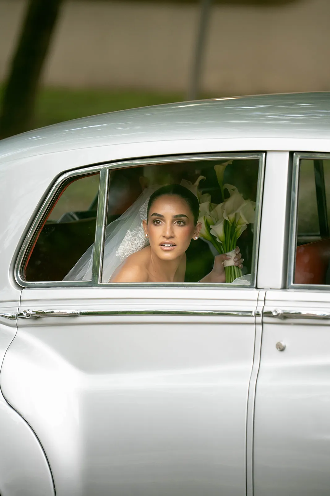 Bride with calla lilies looking out the window of a white vintage car