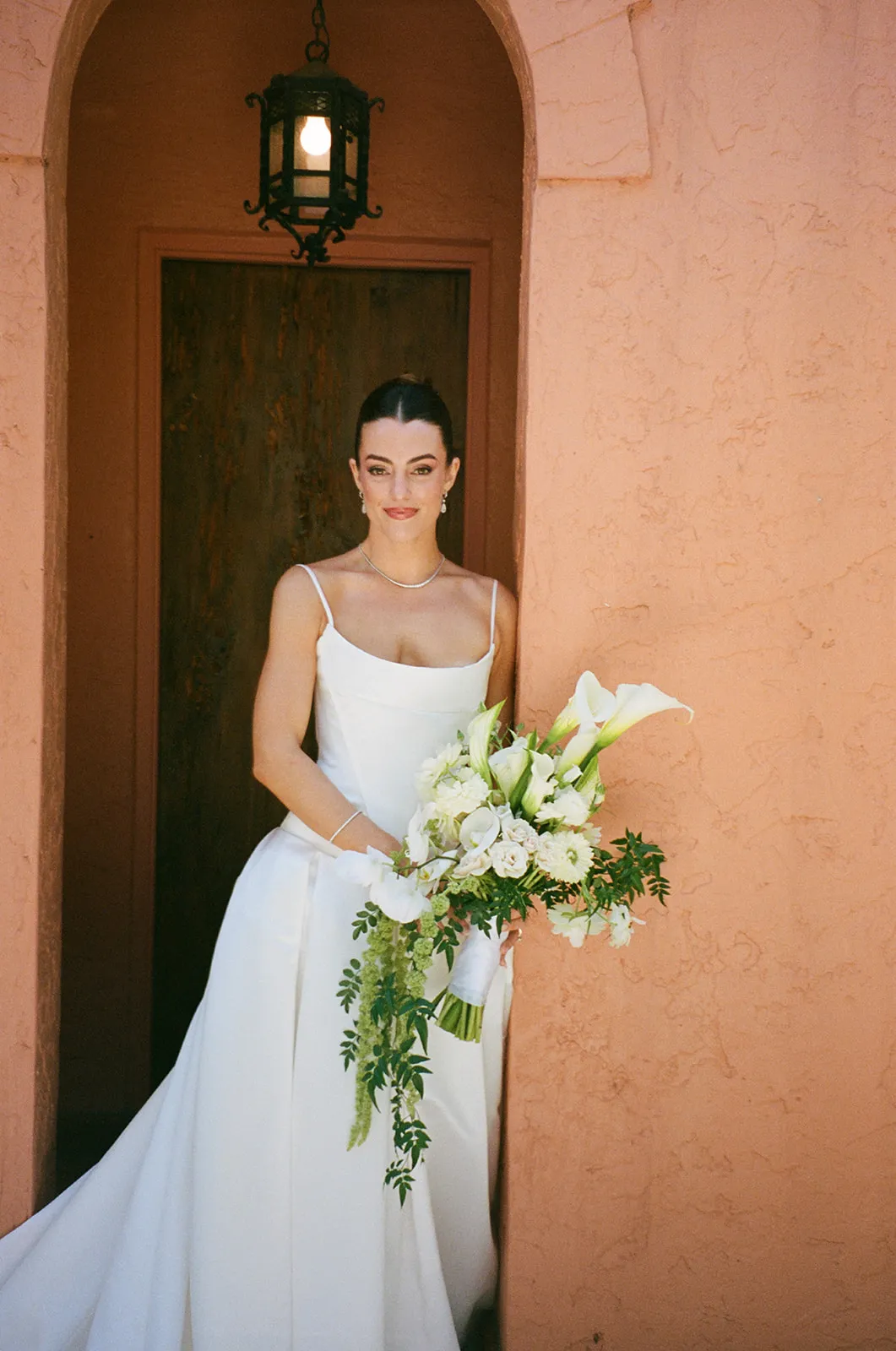 Bride with a white calla lily bouquet in a doorway of a pink stucco wall