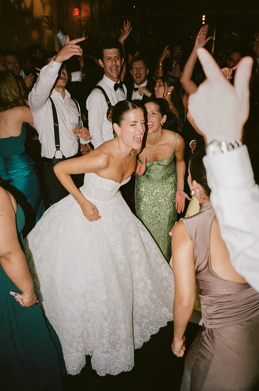 Bride laughing mid-dance in a crowded reception with guests cheering