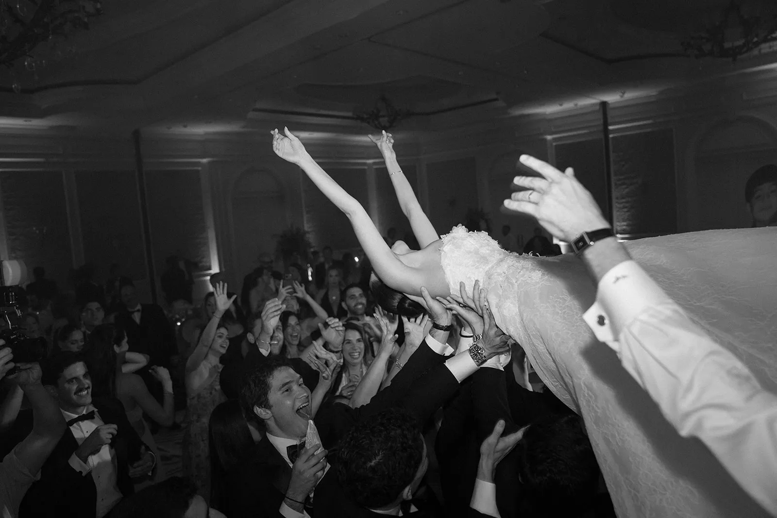 Bride lifted overhead by cheering guests on the dance floor, in black and white