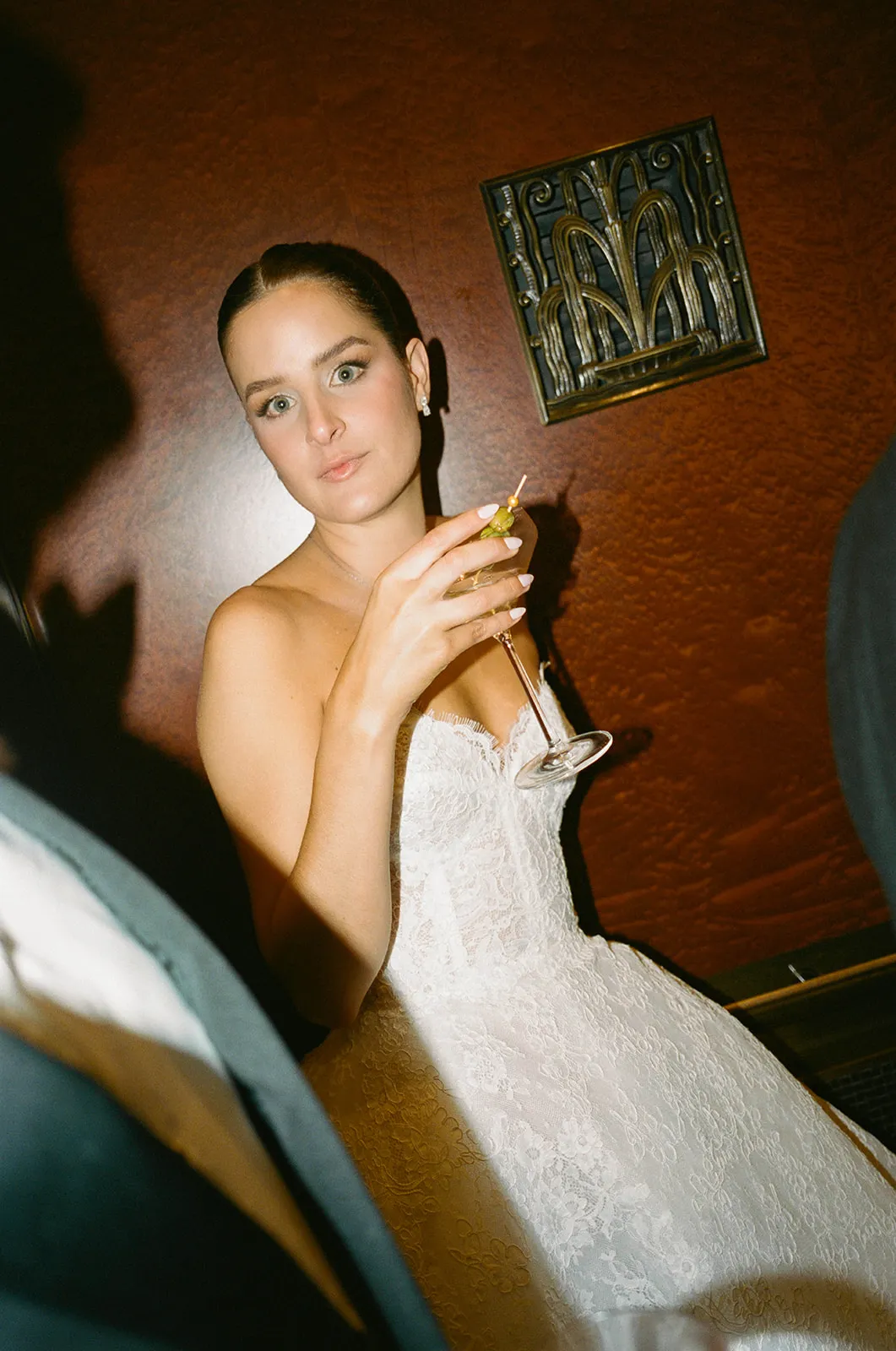 Bride in a strapless lace gown holding a martini against a red wall