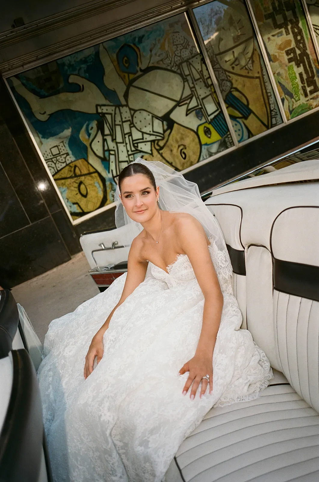 Bride in a veil and lace ball gown seated in a vintage convertible