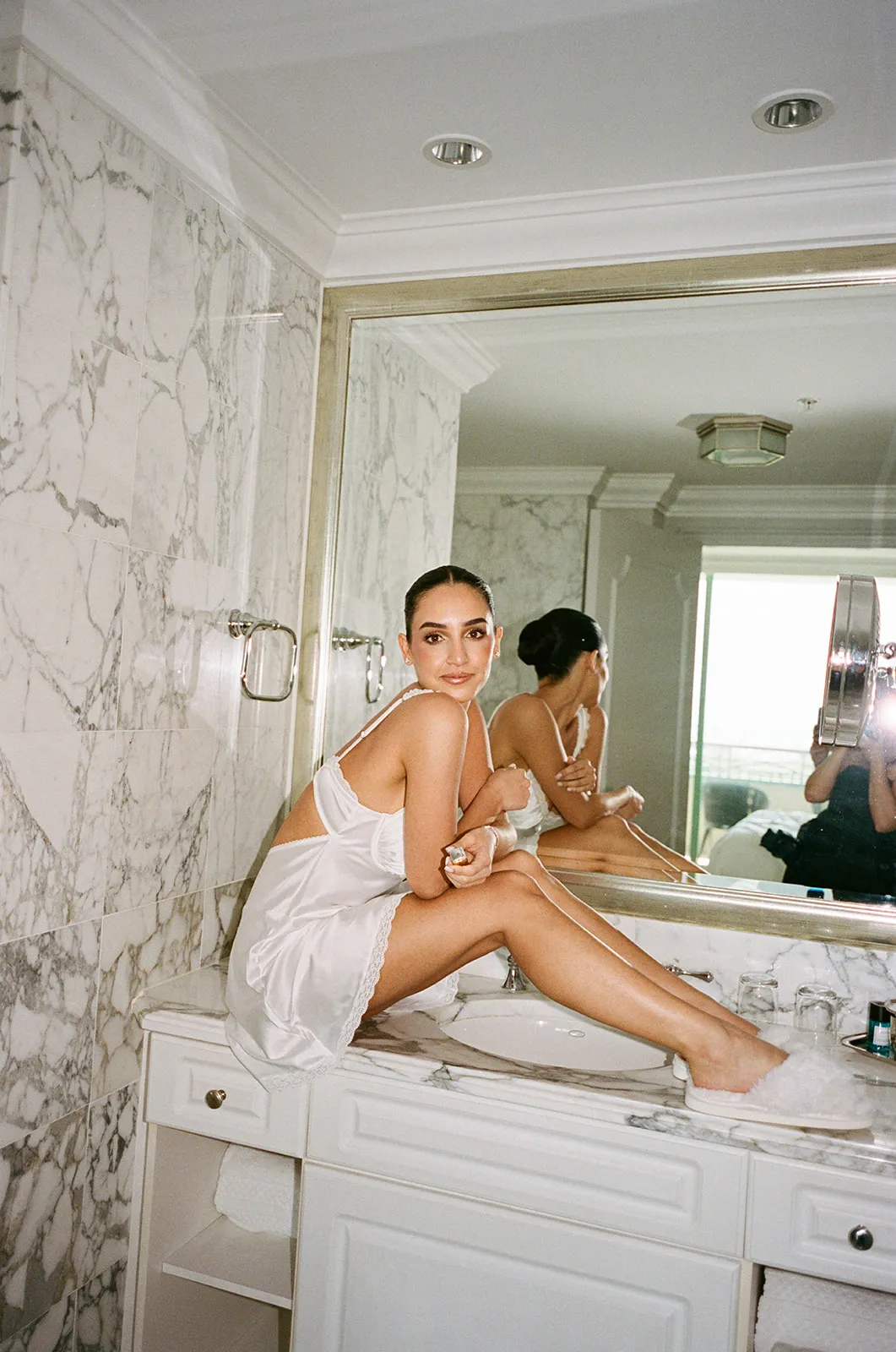 Bride in a white slip perched on a marble bathroom counter