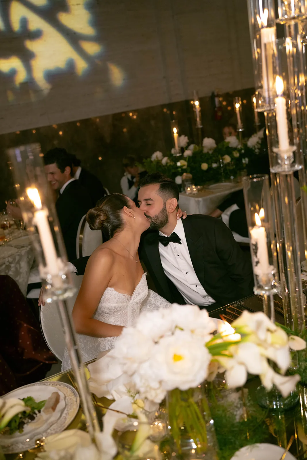 Bride and groom kissing at their table behind candles and white flowers