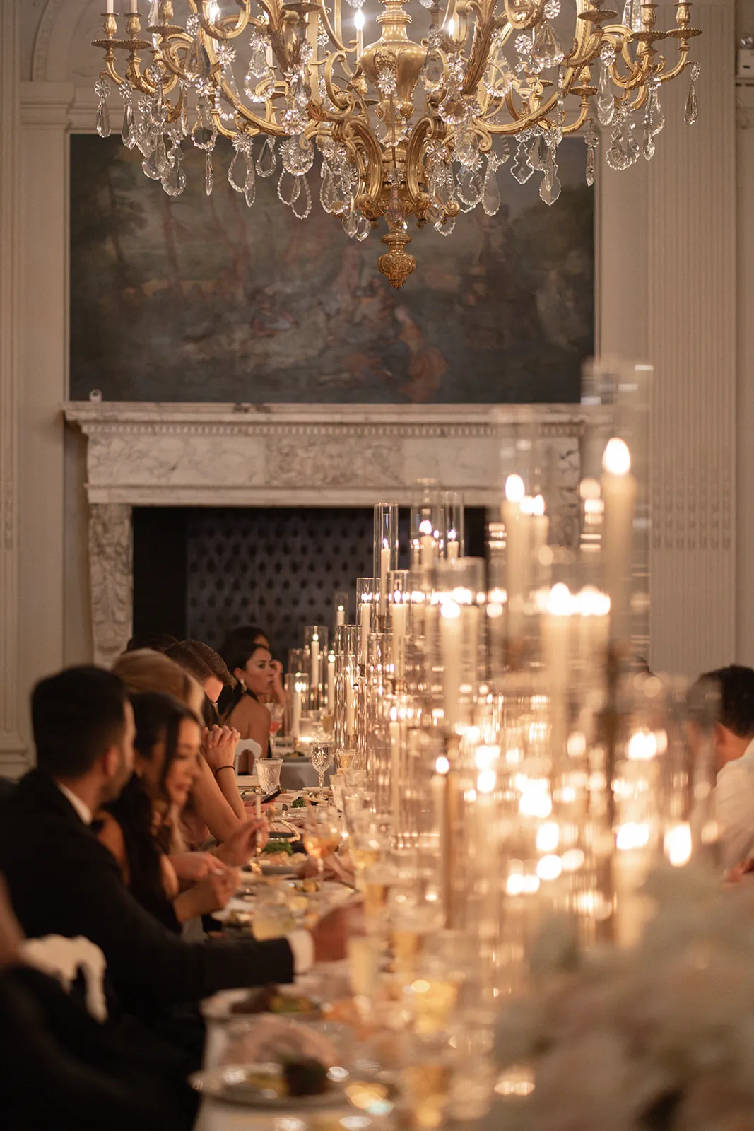 Guests dining beneath a crystal chandelier along a table of tapered candles