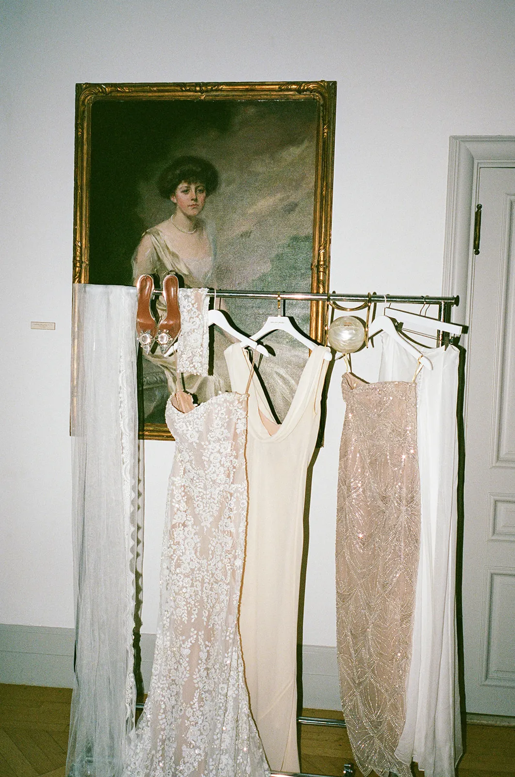 Beaded and silk dresses on a garment rack in front of an antique portrait